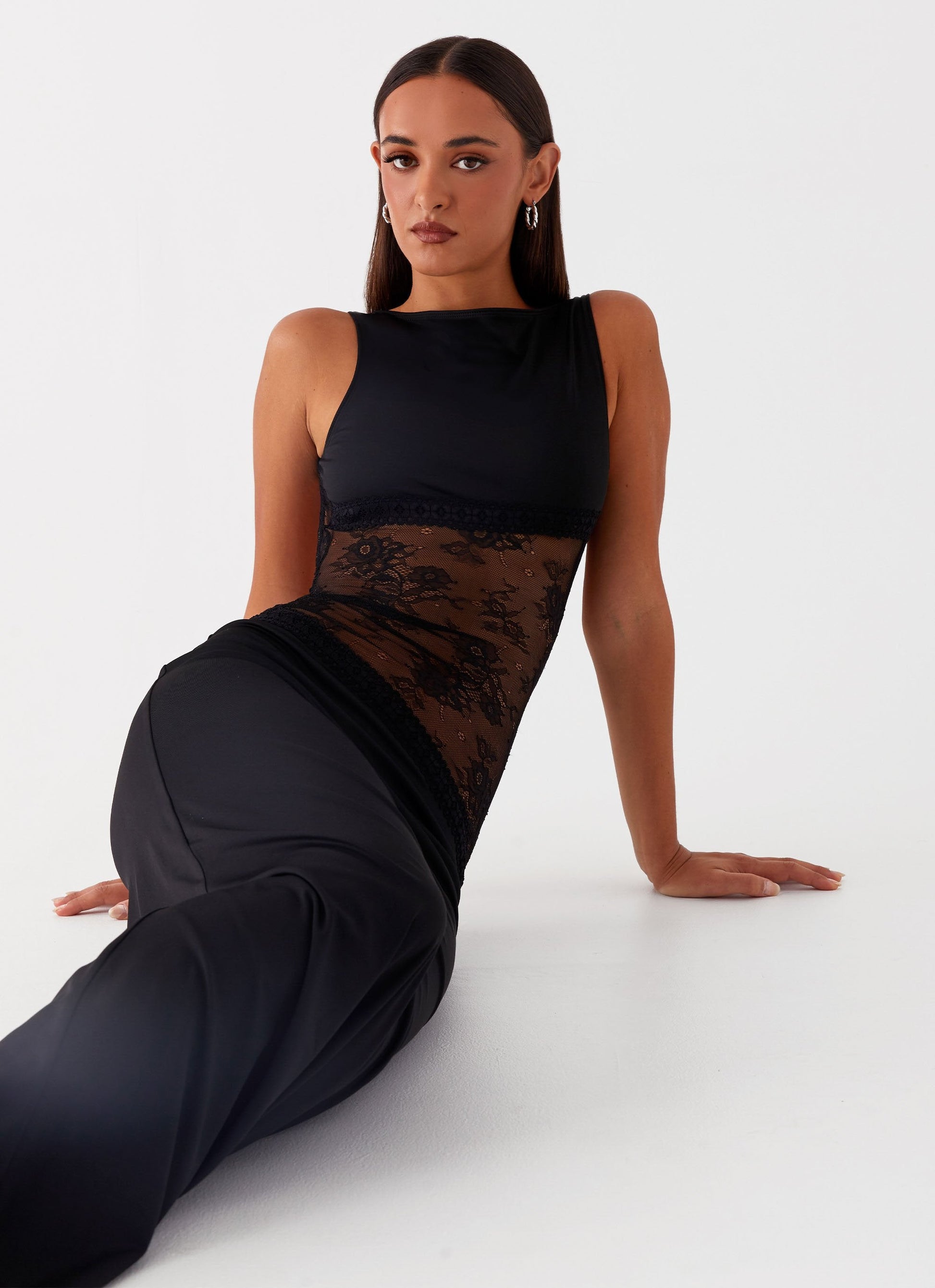 Black Camille Lace Maxi Dress with sheer lace midsection, worn by a seated model, showing full length.