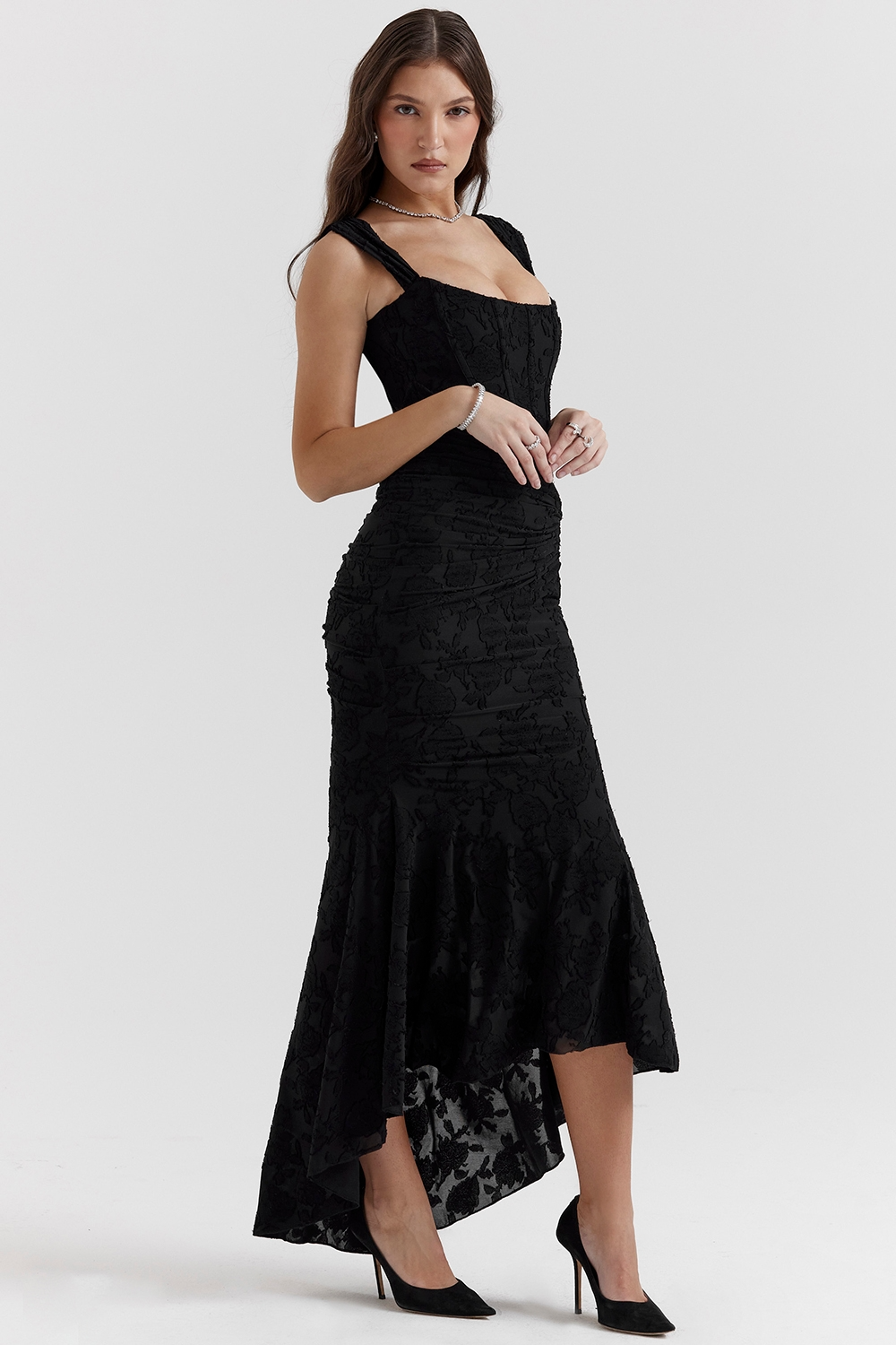 Black floral jacquard corset maxi dress with ruched detailing and high-low hem, paired with black pointed heels.