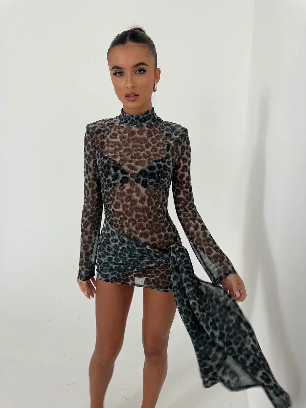 Front view of the Carina Ruched Mini Dress, showcasing the sheer dark grey and black animal print, high neck, and long sleeves with a flowing ruched side detail.