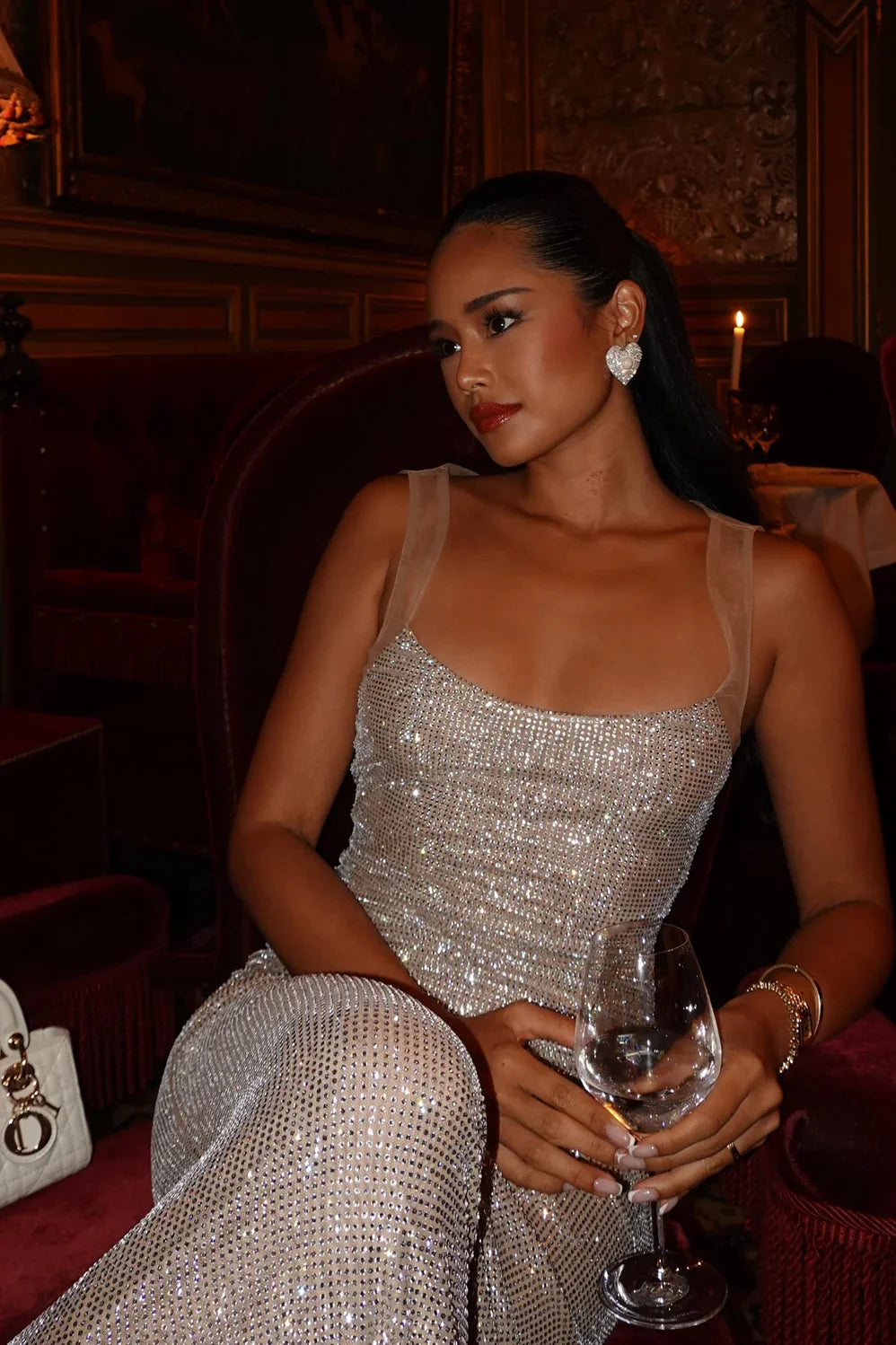 Close-up of the sequined bodice and sheer straps of the Caroline Sequin Maxi Dress, with a woman holding a wine glass.