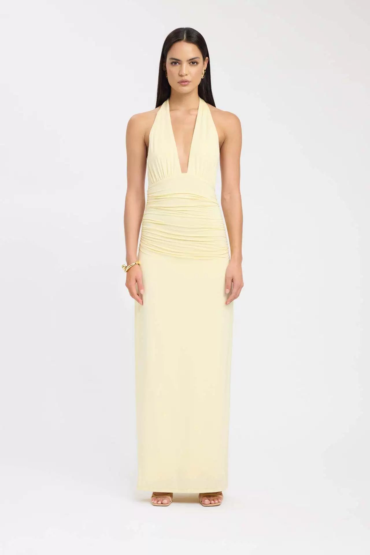 Pale yellow ruched maxi dress with a plunging halter neckline and a fitted bodice, perfect for a special occasion.