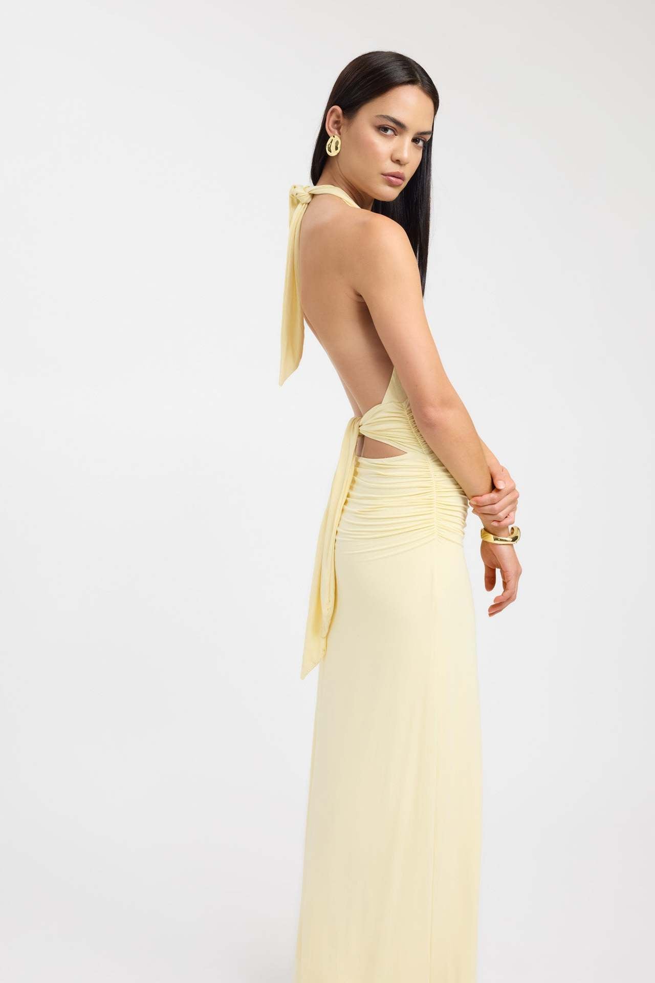 Side view of a pale yellow ruched maxi dress, emphasizing the open back with tie details and gathered waist.