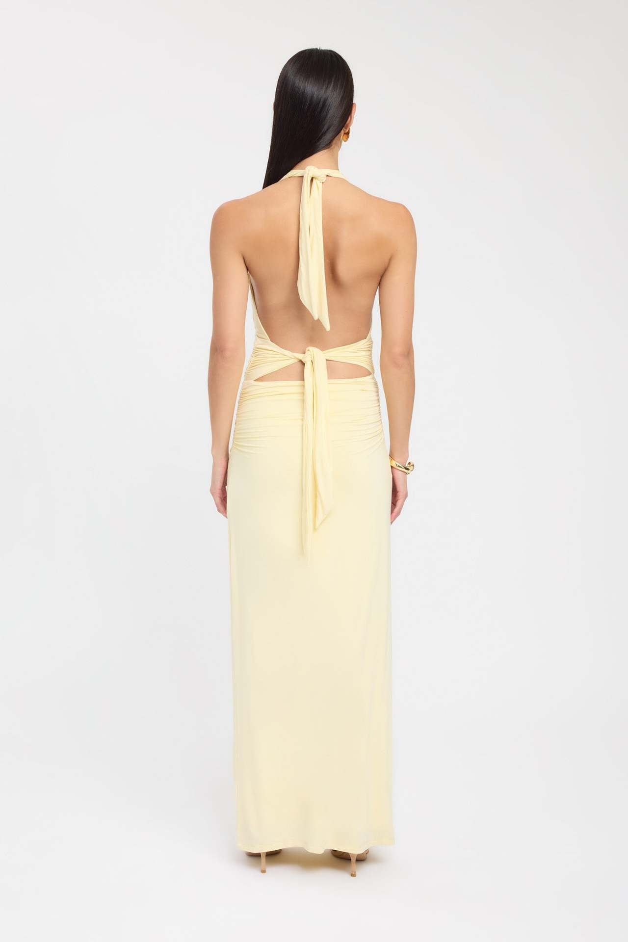 Back view of a light yellow ruched maxi dress, featuring a halter neck with ties and a subtly ruched back.
