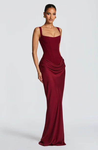 Side profile of a rich burgundy Celeste corset maxi dress, showcasing the silhouette and draped fabric.