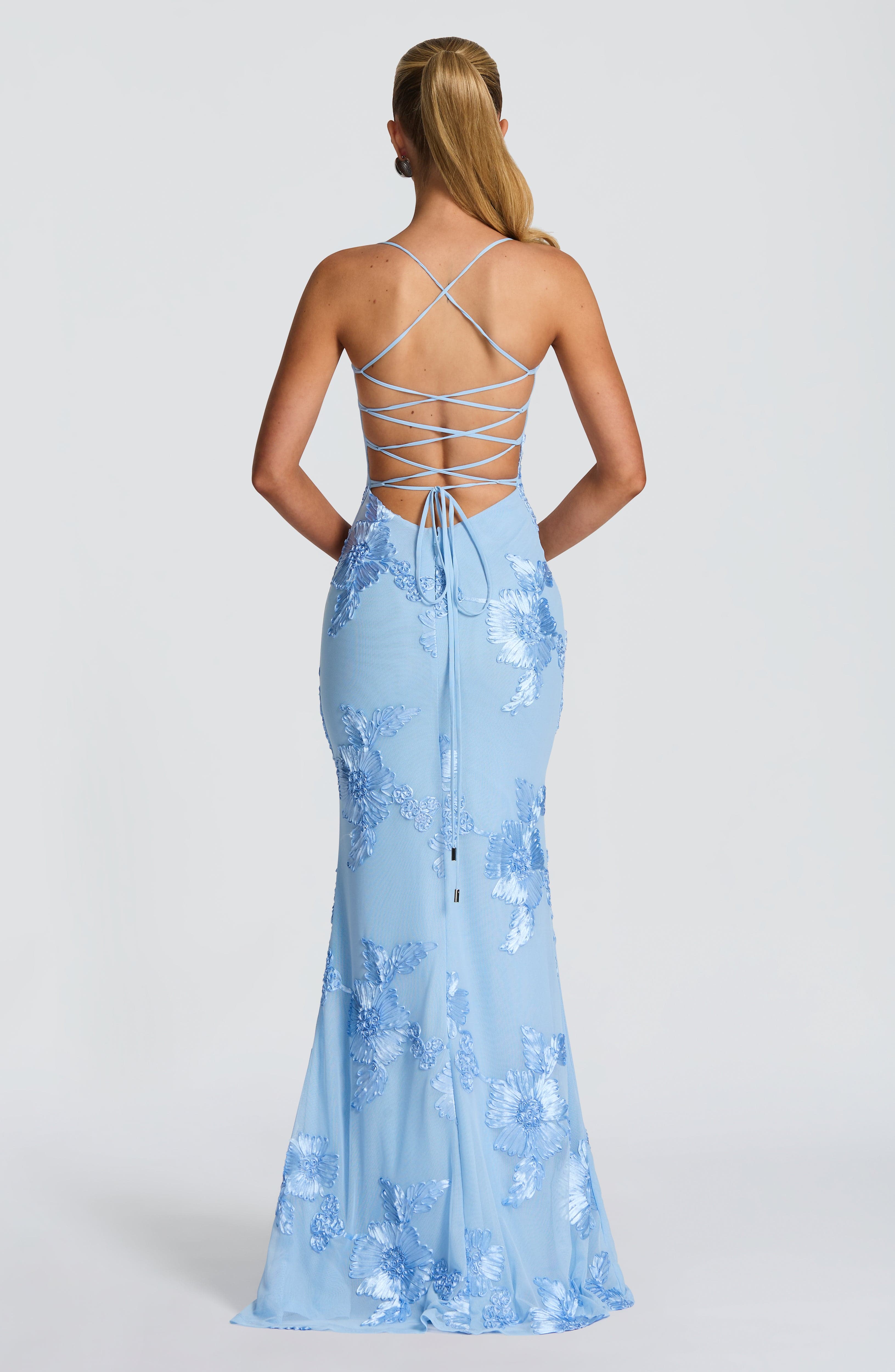 Back view of a light blue floral maxi dress showcasing a criss-cross lace-up design, an open back, and embroidered floral details on the skirt.