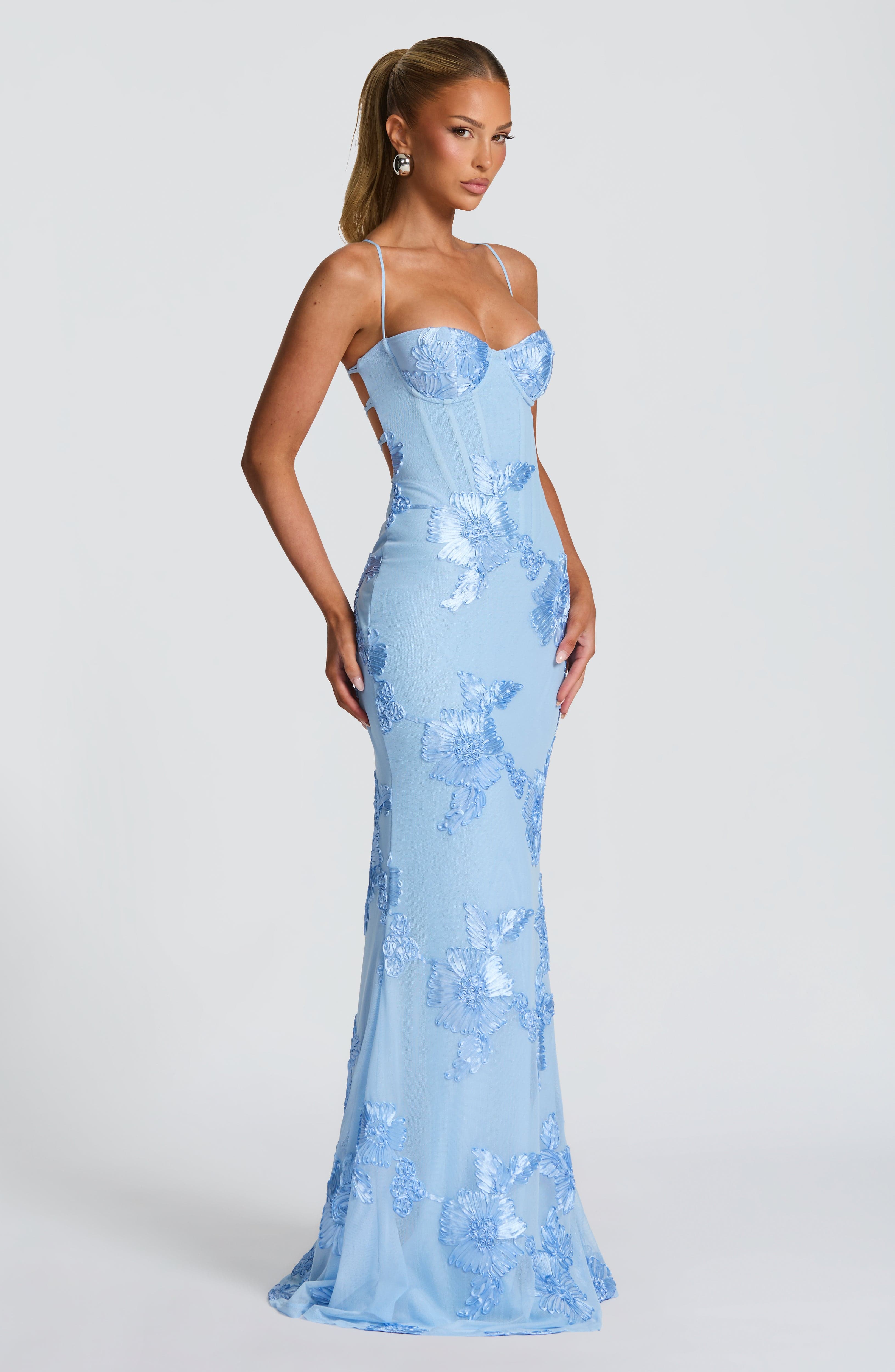 Side profile of a light blue floral maxi dress with a fitted silhouette, thin straps, and an elegant flared hem, featuring intricate floral embroidery.