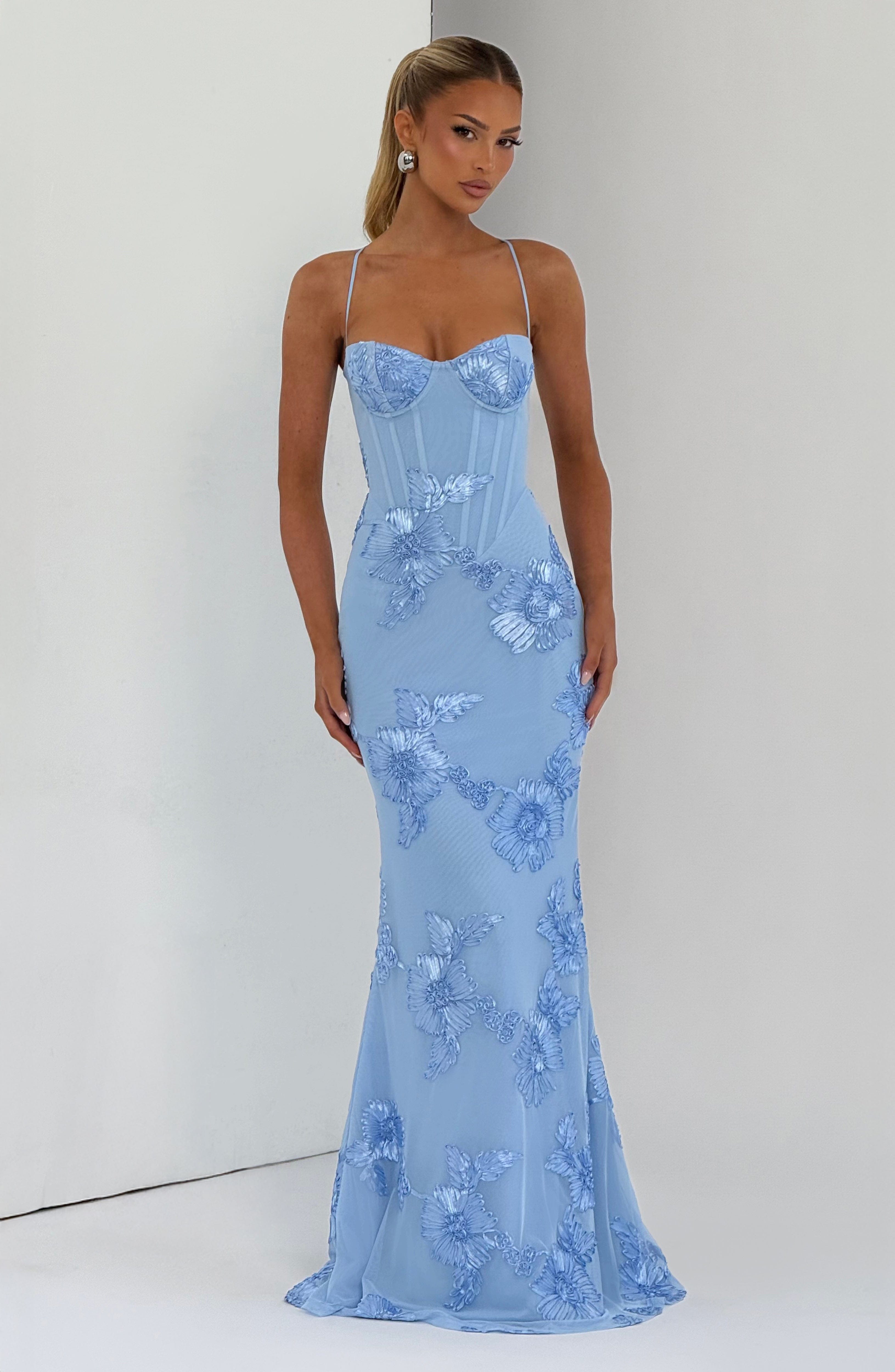 Full-length view of a light blue floral maxi dress with a subtle train, delicate straps, and a fitted silhouette, showcasing the detailed floral embroidery.