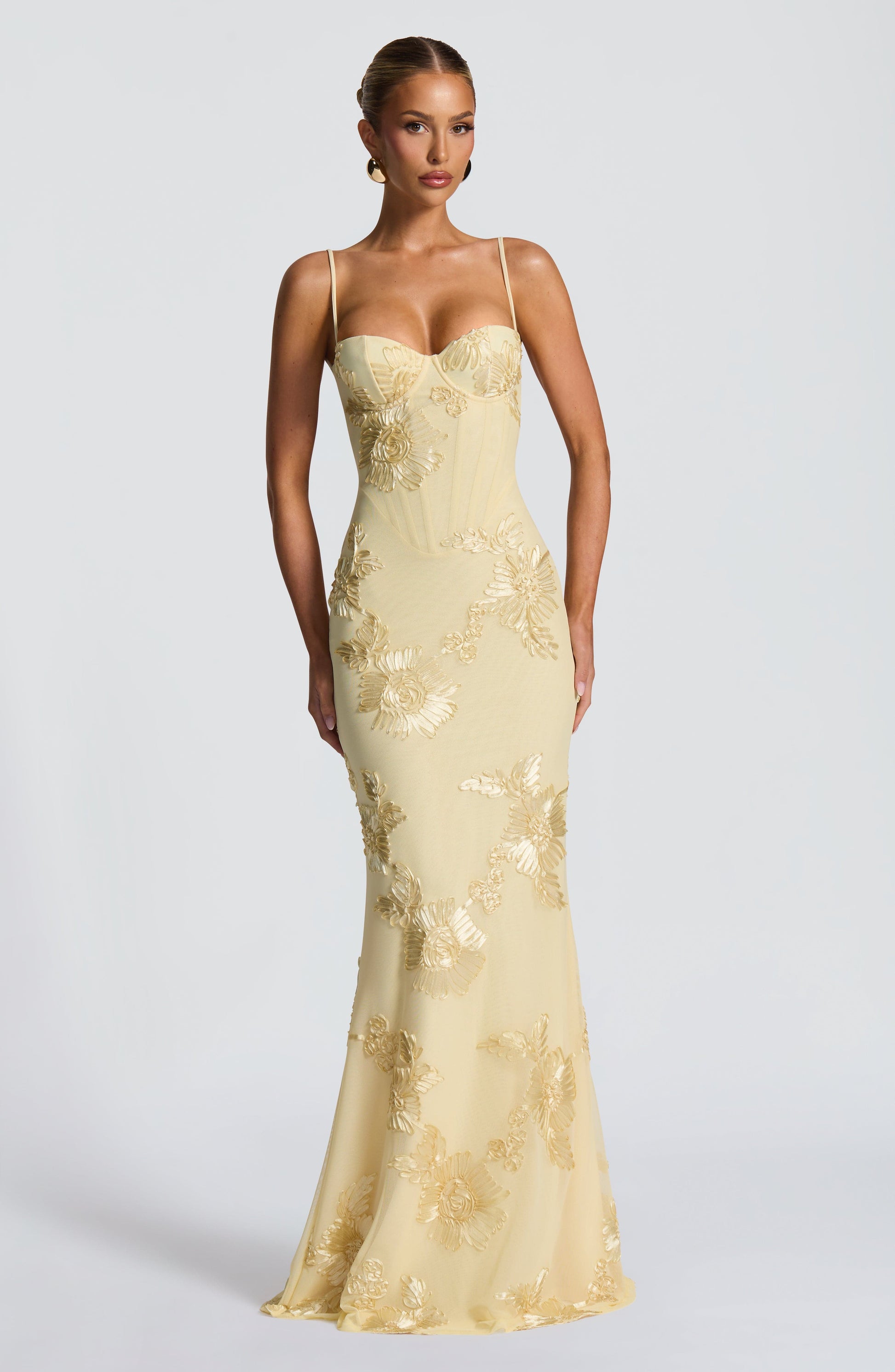 Front view of a woman in a light yellow Celestina floral maxi dress, featuring a structured bodice with gold floral embroidery and a fitted silhouette.