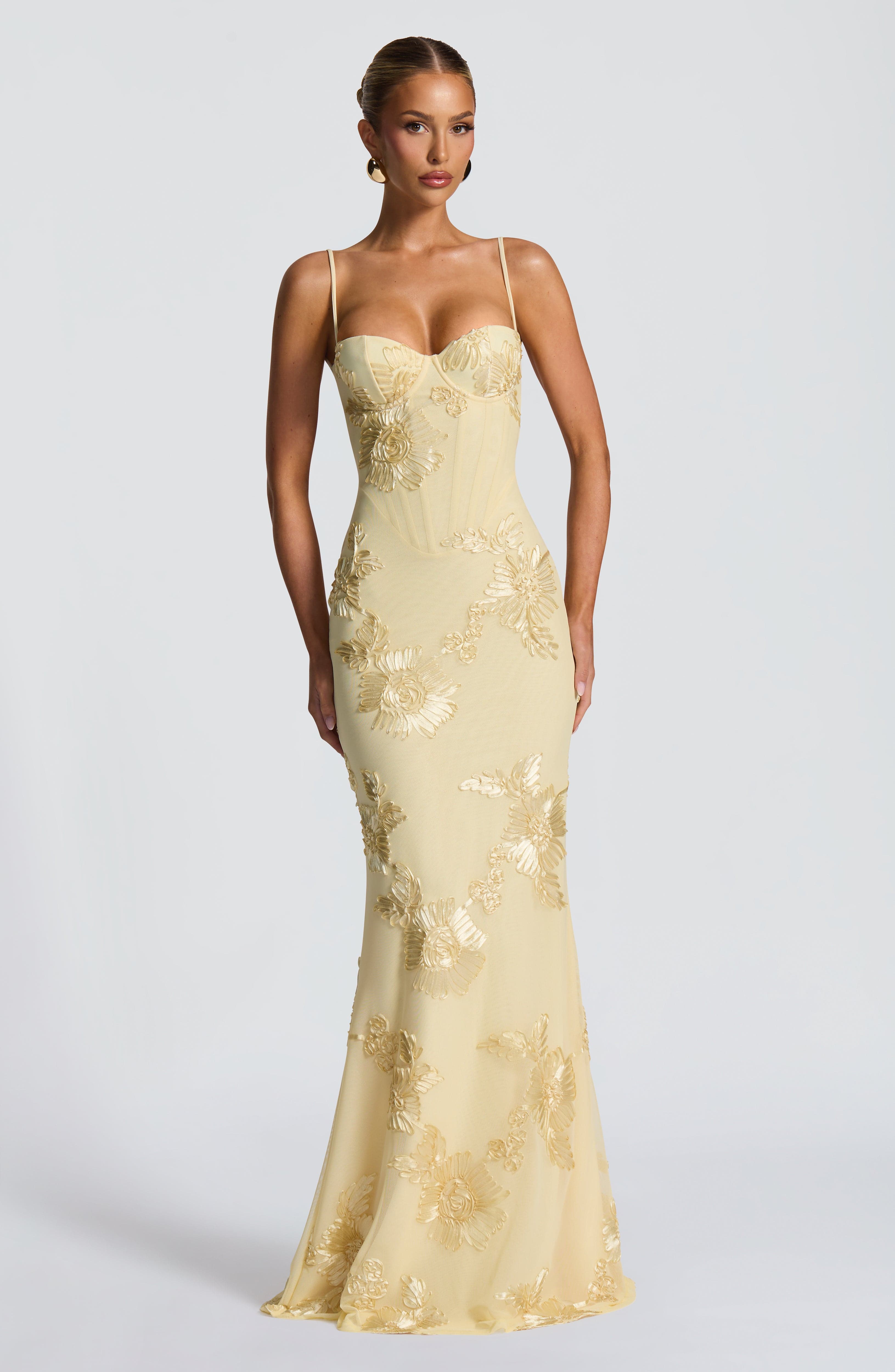 Front view of a woman in a light yellow Celestina floral maxi dress, featuring a structured bodice with gold floral embroidery and a fitted silhouette.