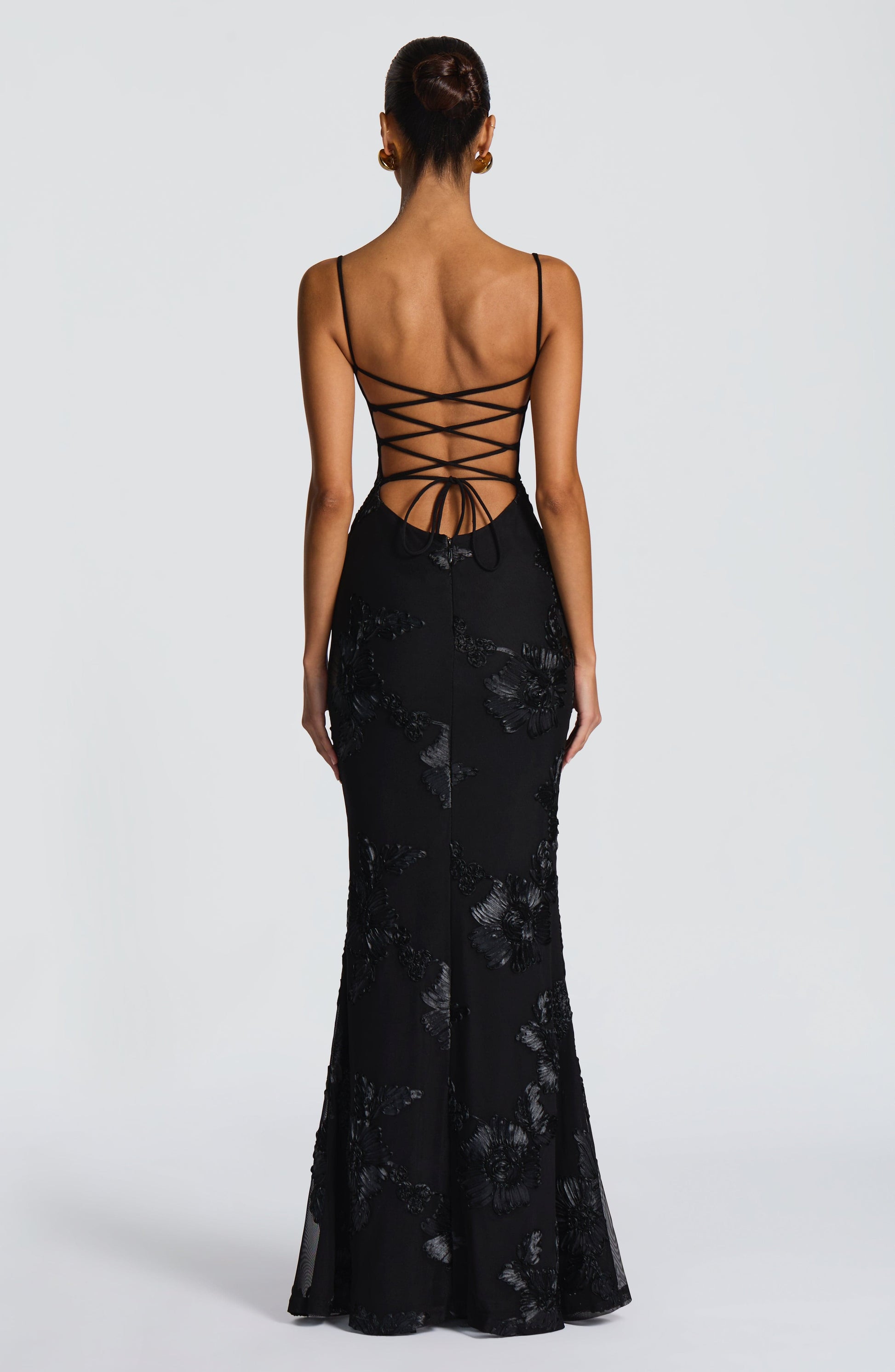 Back view of the black Celestina Floral Maxi Dress, showcasing a lace-up back design and elegant floral appliqué down the skirt.