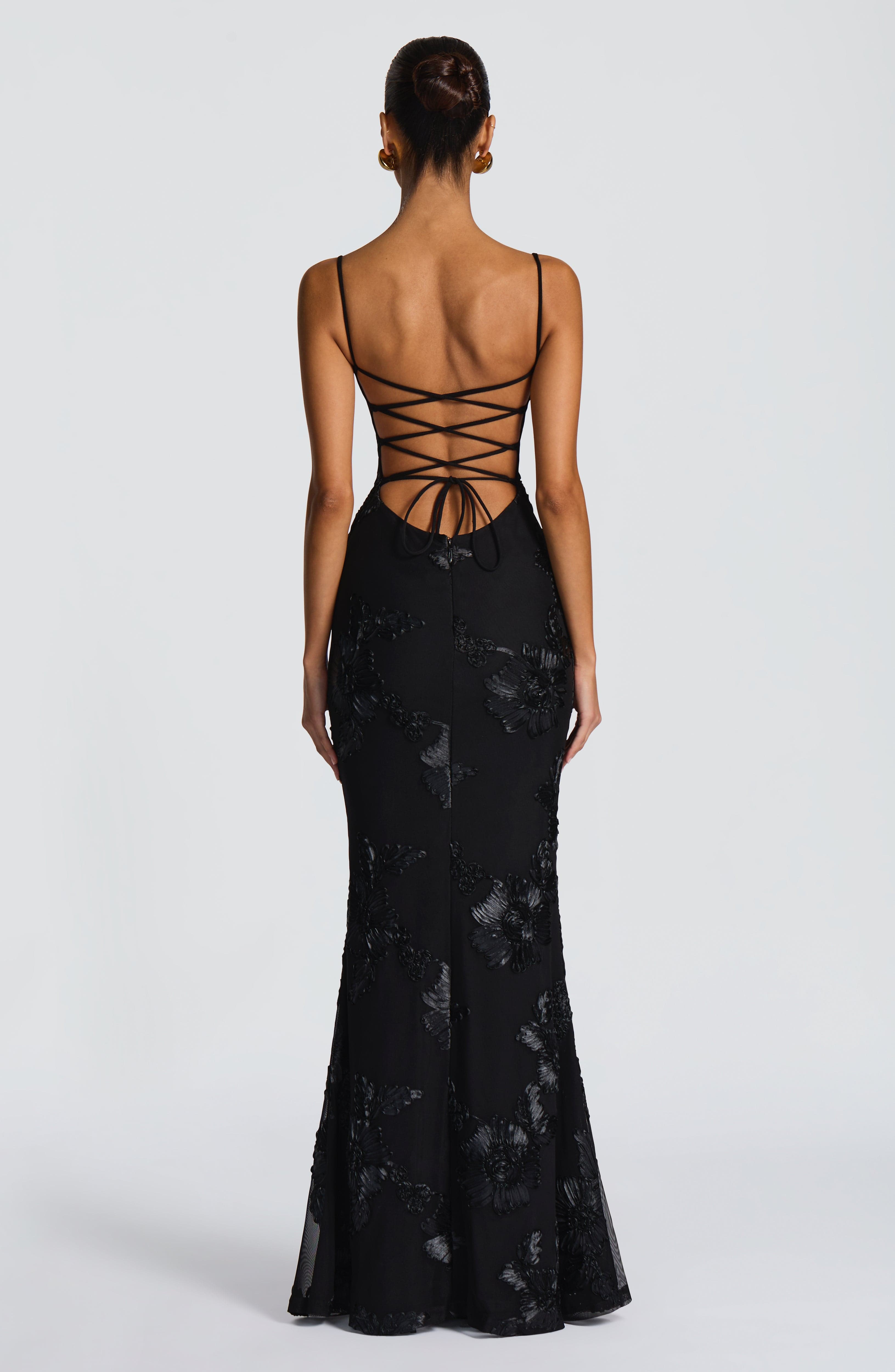 Back view of the black Celestina Floral Maxi Dress, showcasing a lace-up back design and elegant floral appliqué down the skirt.