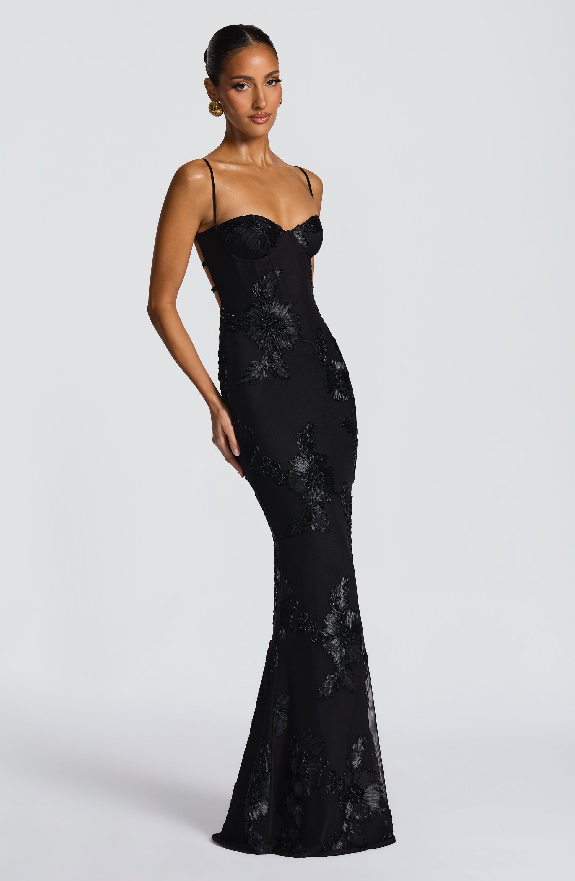 Side view of the black Celestina Floral Maxi Dress, showing the form-fitting silhouette and a subtle train with floral embellishments.