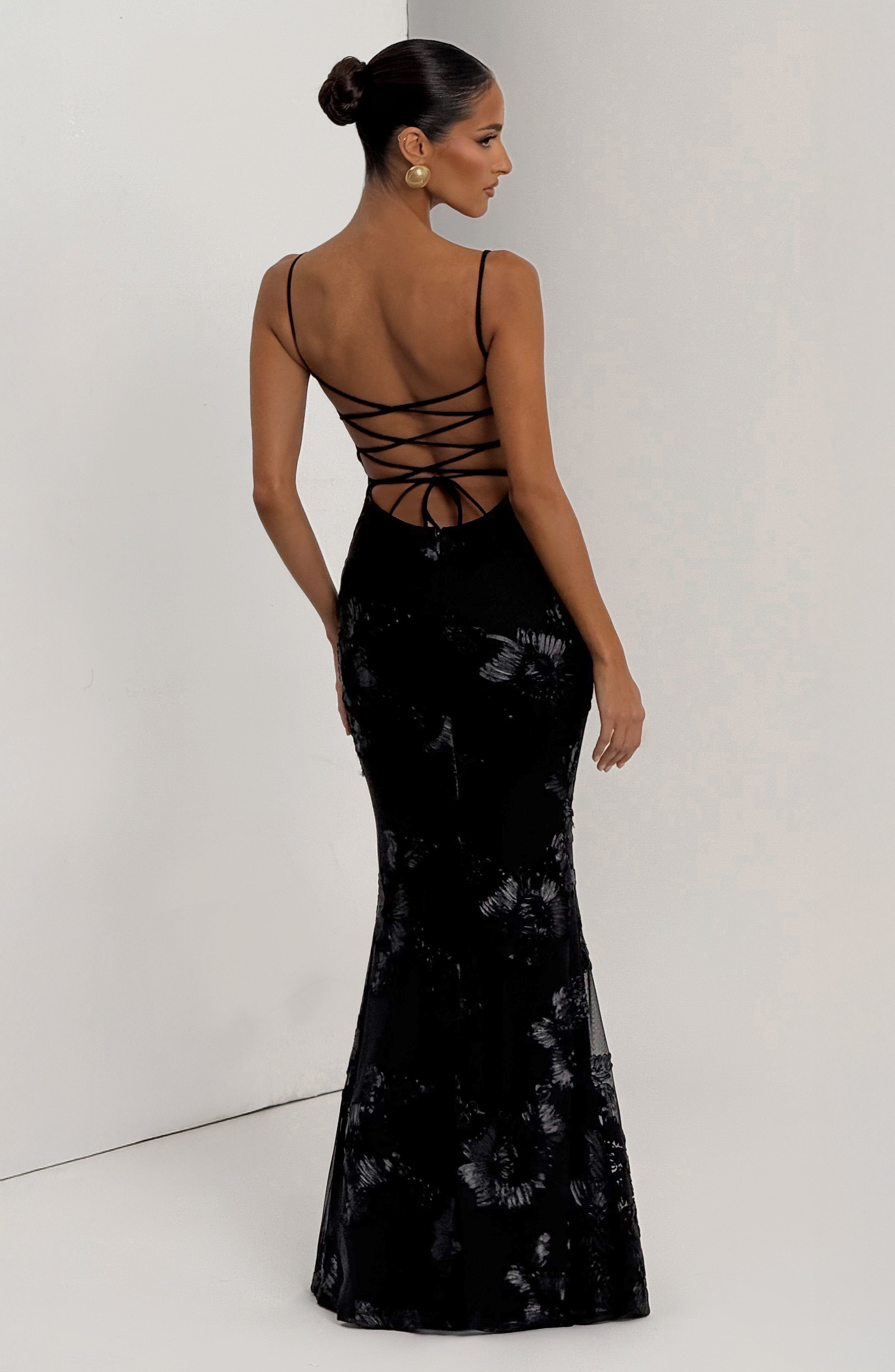 Back view of the black Celestina Floral Maxi Dress, highlighting the lace-up detail and the flowing skirt with scattered floral embellishments.