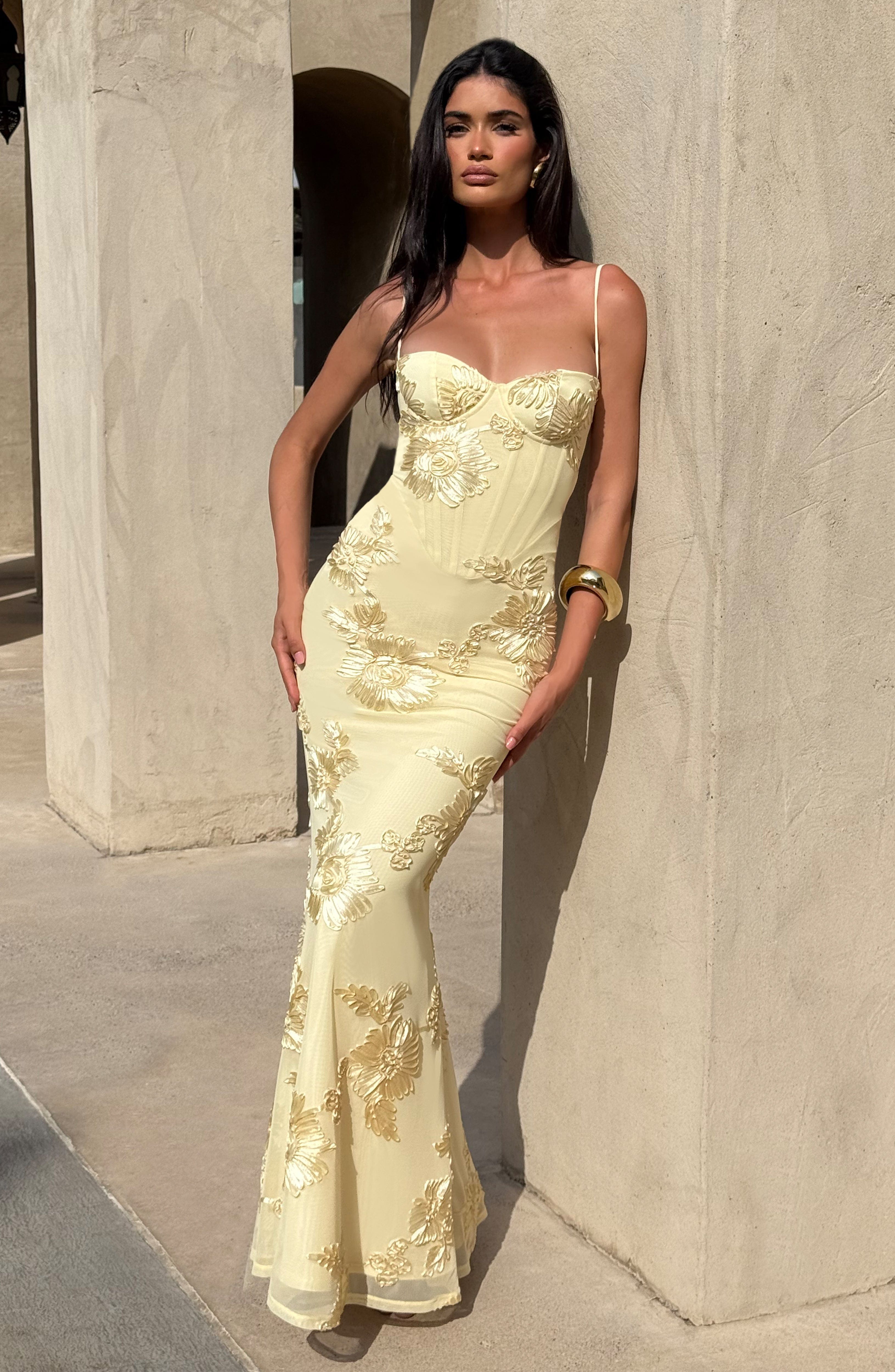 Full body shot of a woman posing in the light yellow Celestina floral maxi dress, showing the elegant fit and detailed gold floral patterns.