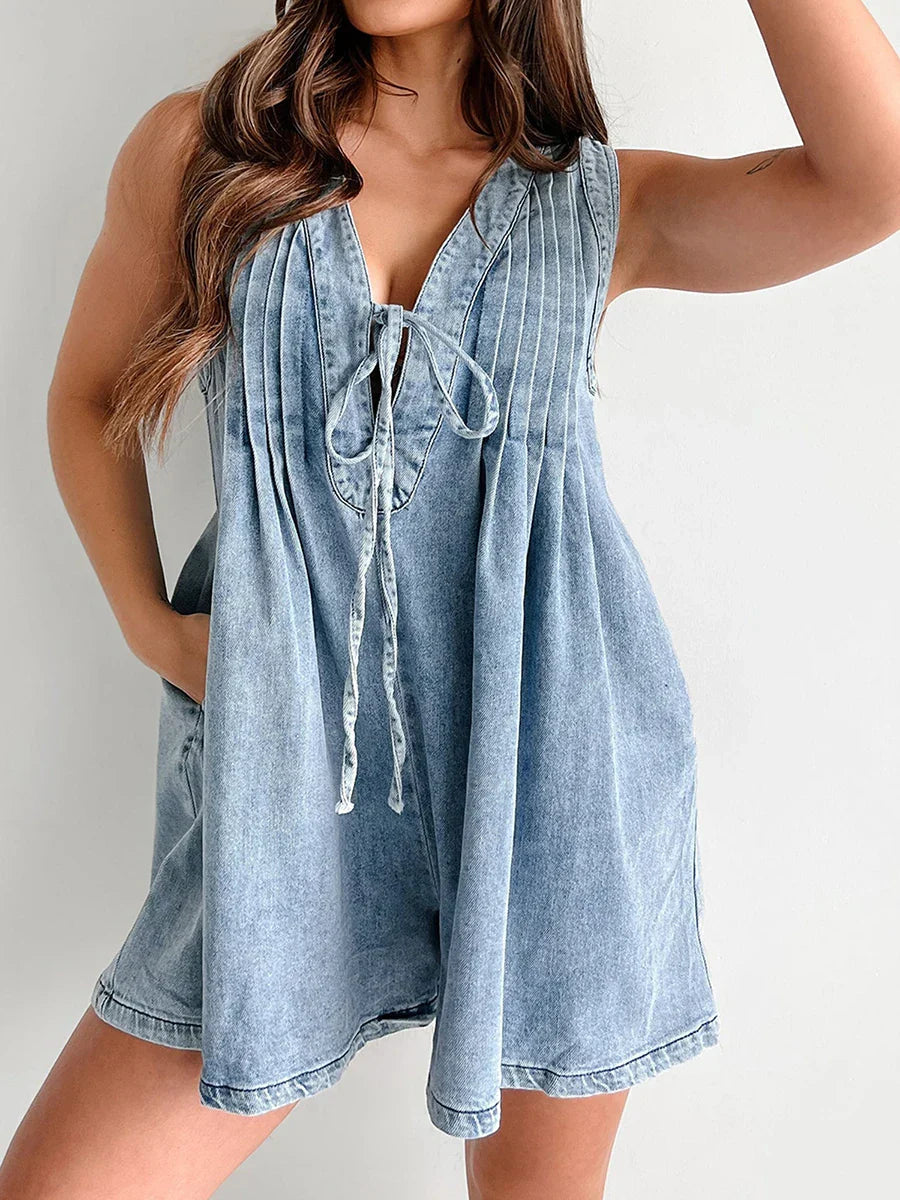 Light wash denim mini dress with a v-neckline, tie-front detail, and pleated bodice, featuring a relaxed fit.