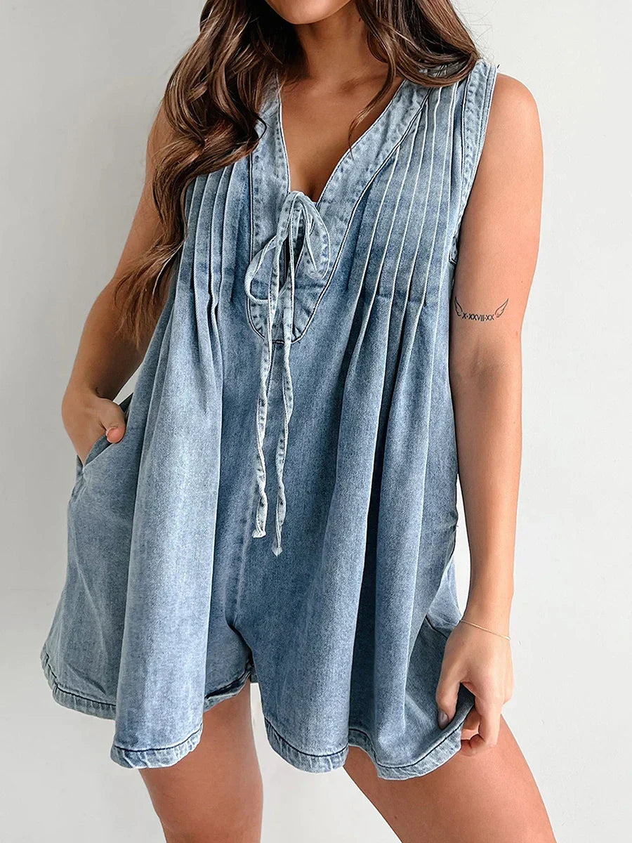 Close-up of the light blue denim mini dress, highlighting the tie-front, v-neck, and vertical pleats on the bodice.
