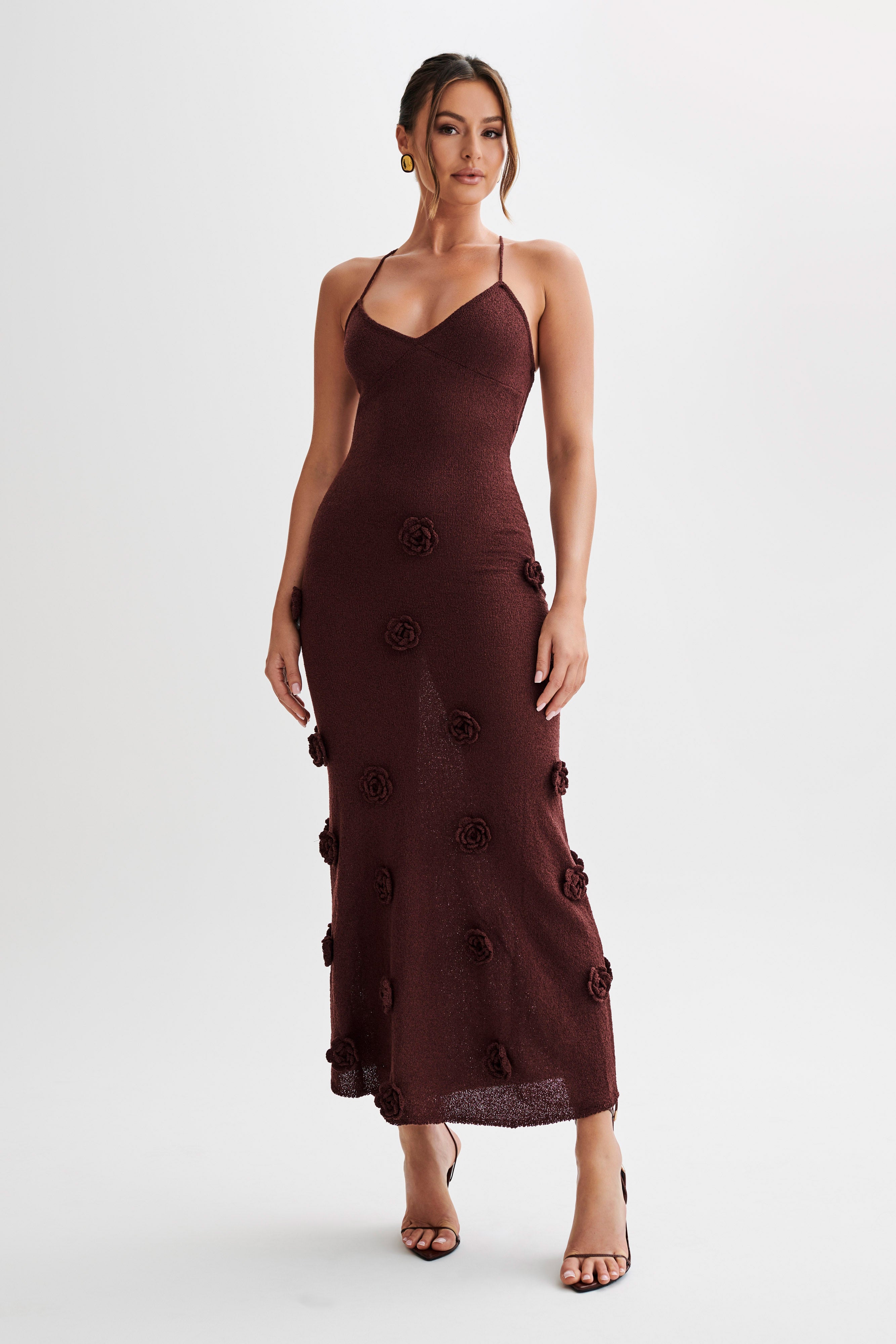 Front view of a dark brown Chelsea Floral Maxi Dress with intricate rose appliques, styled with open-toe heels.
