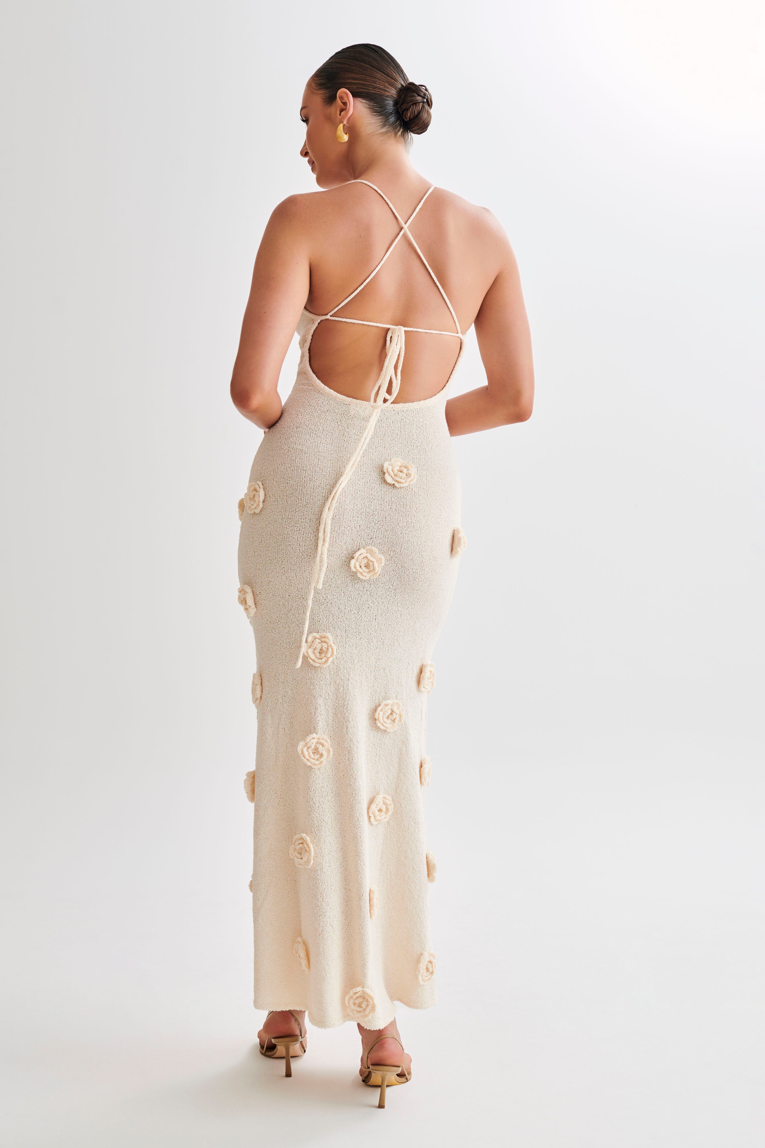 Back view of the cream Chelsea Floral Maxi Dress, highlighting the open back design with criss-cross straps and floral appliques.