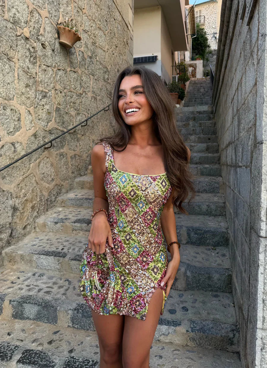 Multicolored mosaic sequin mini dress with square neckline and side slit for women, worn by a model smiling on stone steps.