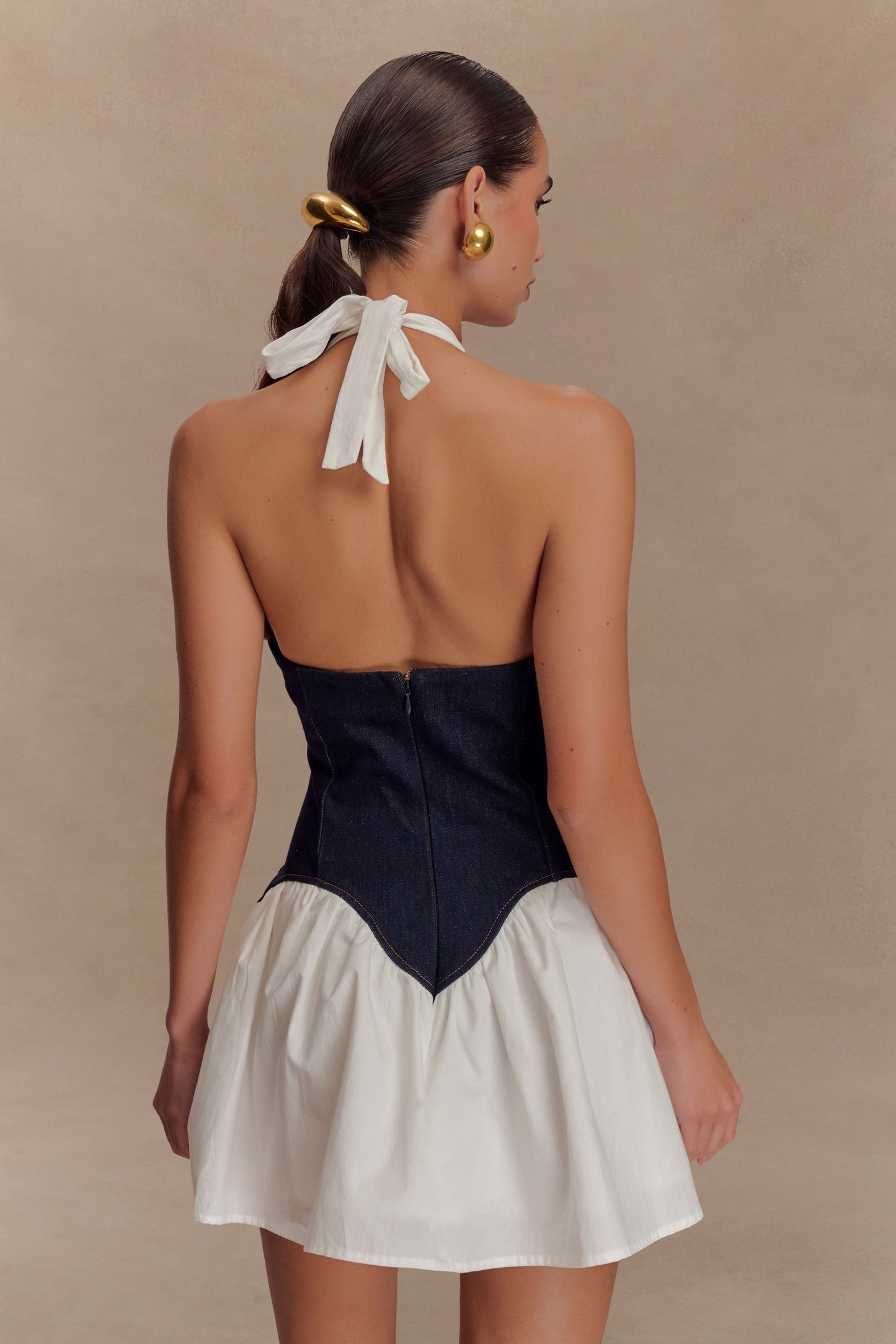 Back view of the Christina mini dress, showing the white halter neck tie, dark denim corset with zipper, and white ruffled skirt.