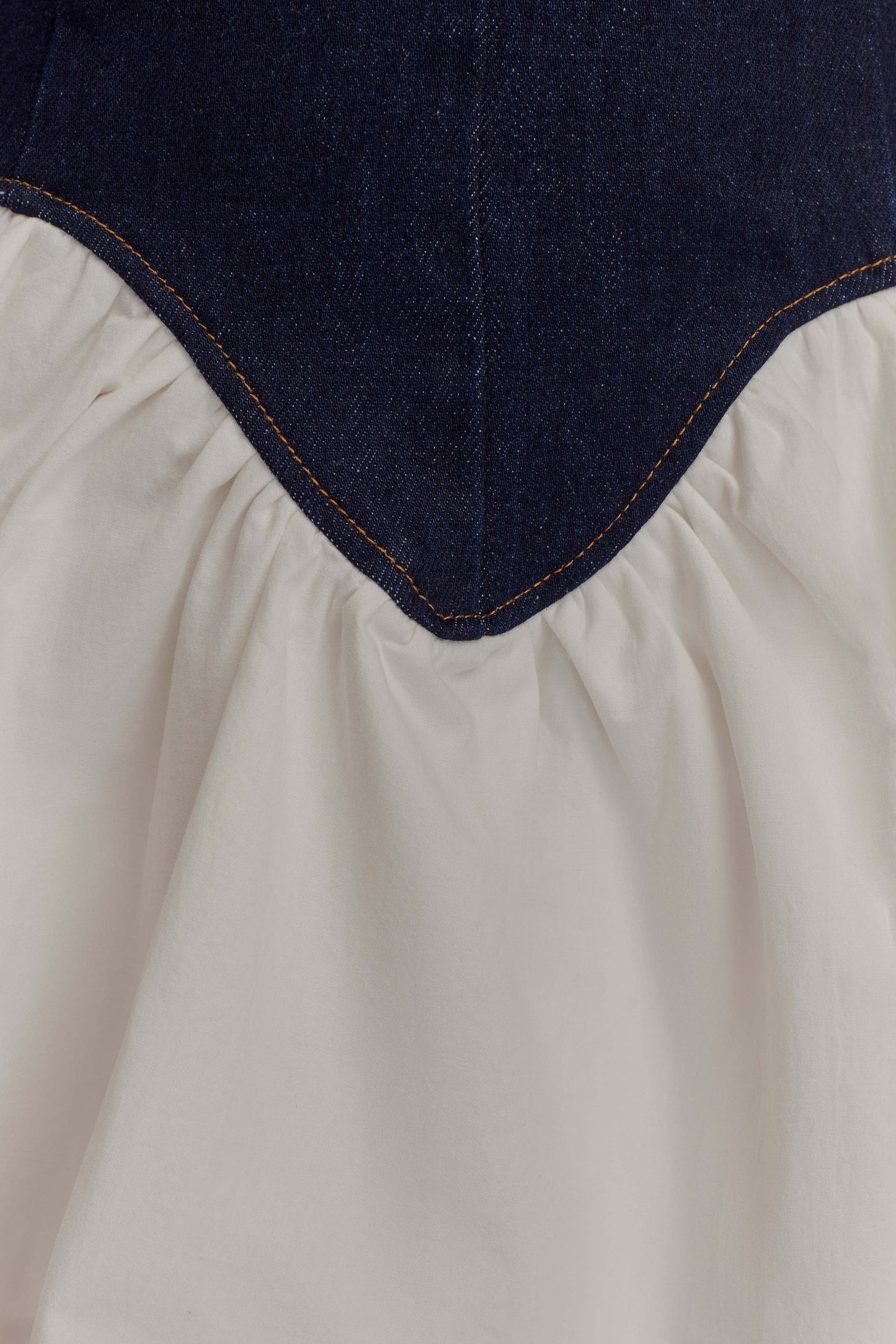 Close-up detail of the Christina mini dress, focusing on the dark denim corset with orange stitching and white ruffled skirt.