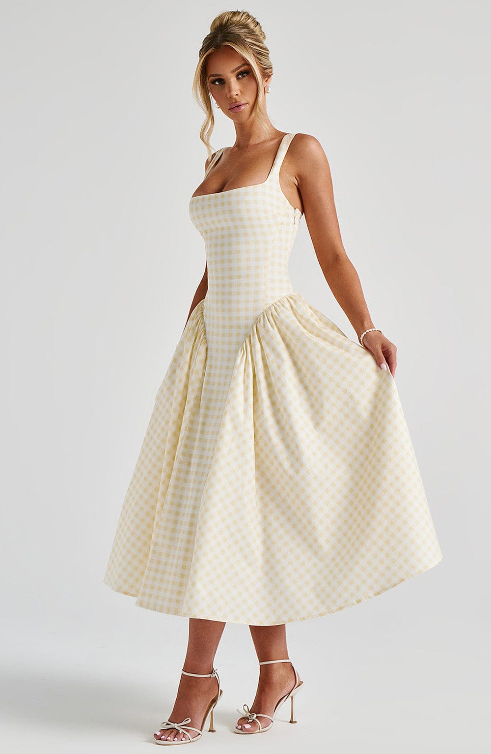 Frontal view of a light yellow gingham midi dress, highlighting the square neckline, fitted bodice, and full skirt with hands in pockets.