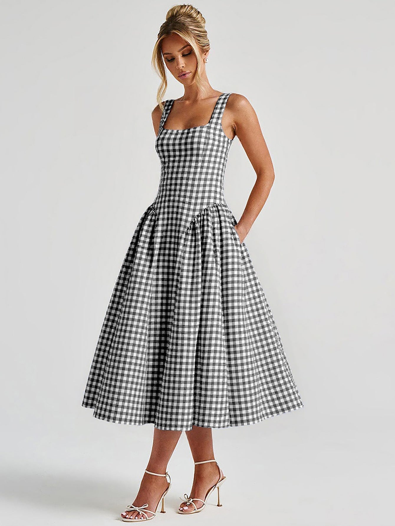 Front view of a black and white gingham midi dress with a square neckline, wide straps, and a full, gathered skirt, paired with white heels.