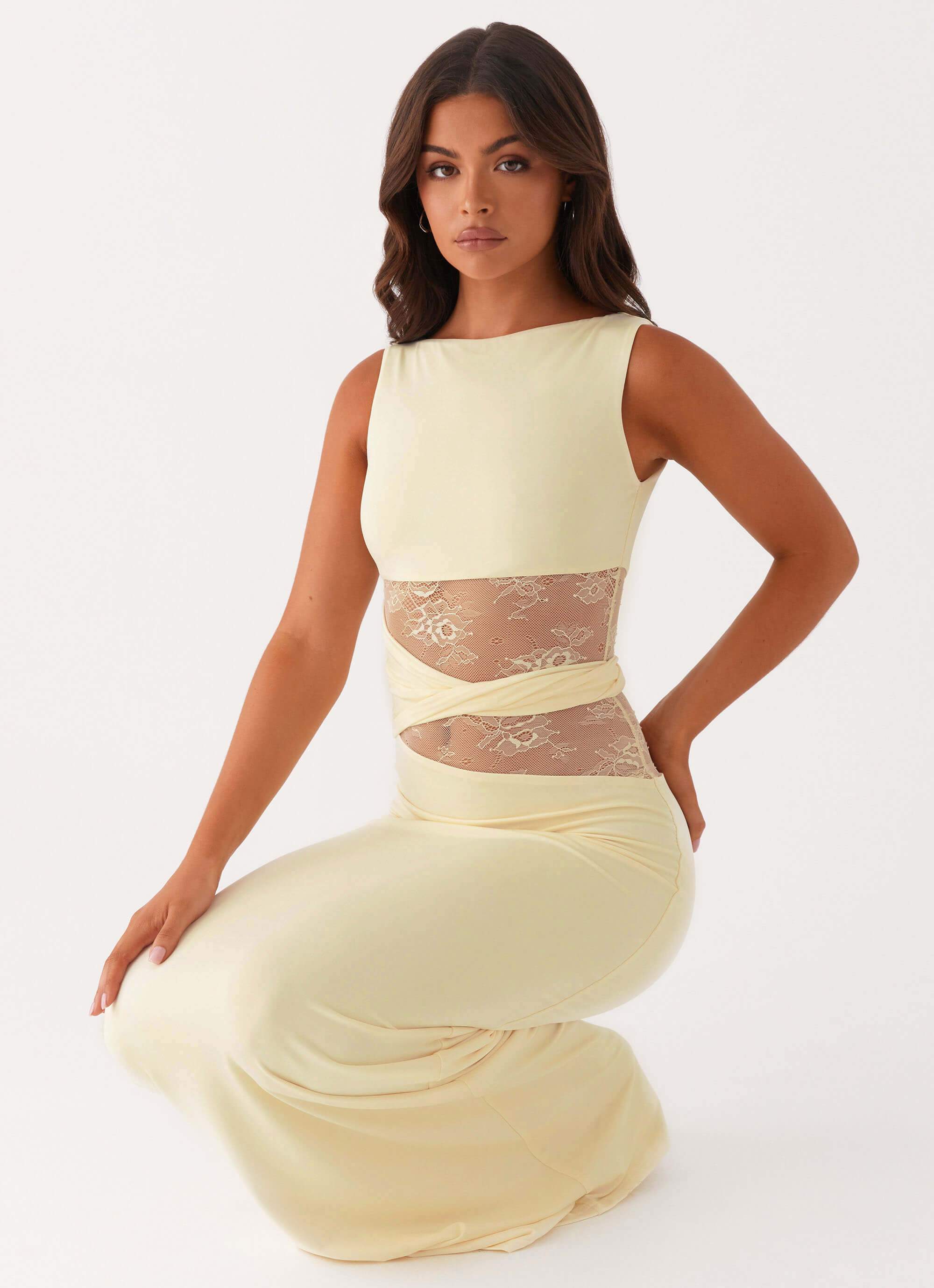Pale yellow Clarisse lace maxi dress featuring sheer cutouts, shown in a crouching pose