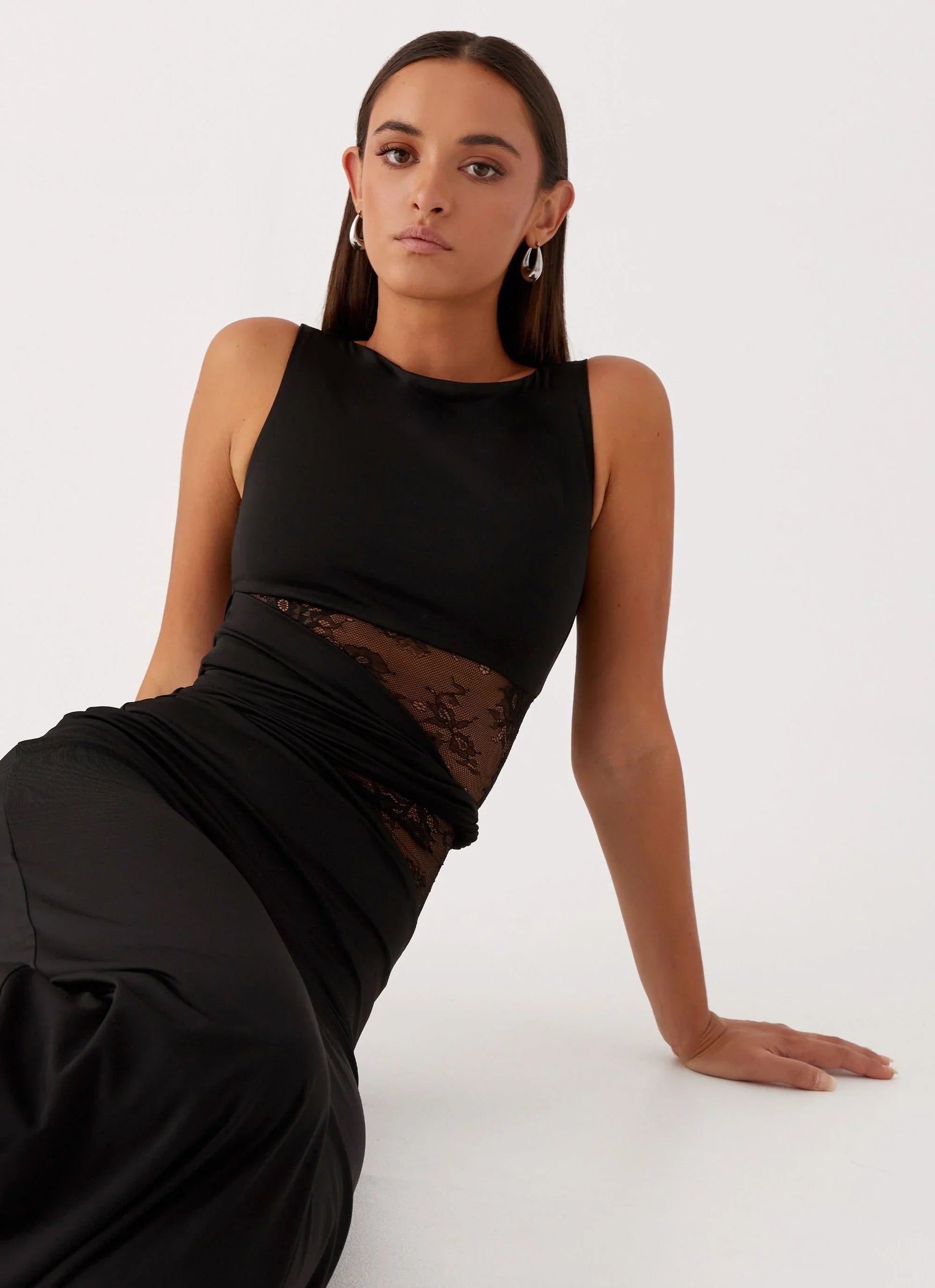 Seated view of a black Clarisse maxi dress, highlighting the boat neck and lace waist details.