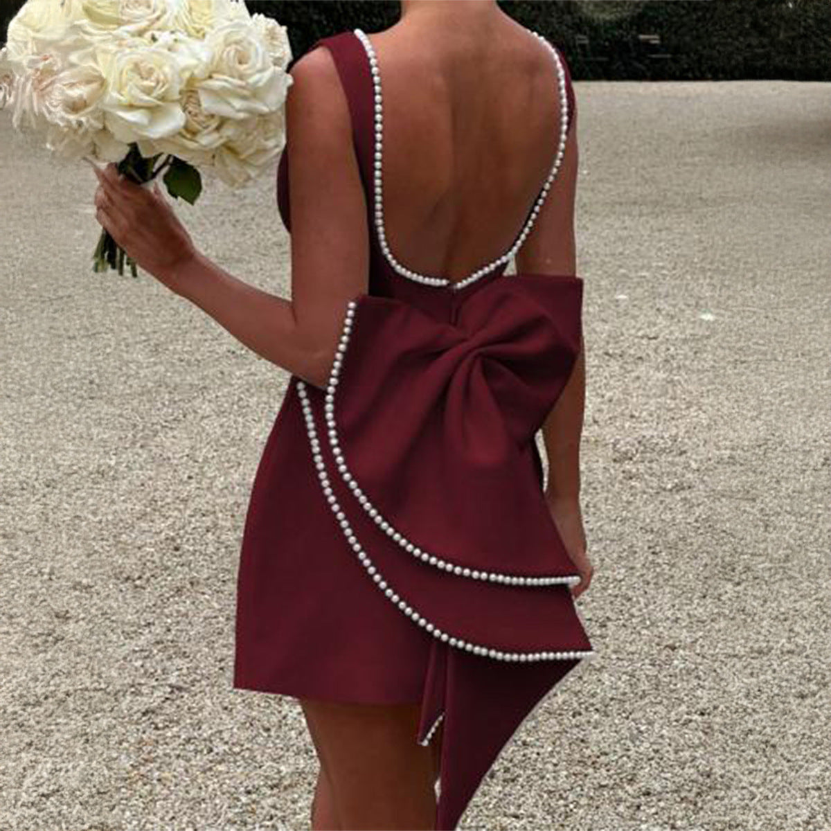 Burgundy mini dress seen from the back, featuring a dramatic pearl-edged bow and a scooped back neckline with pearls.