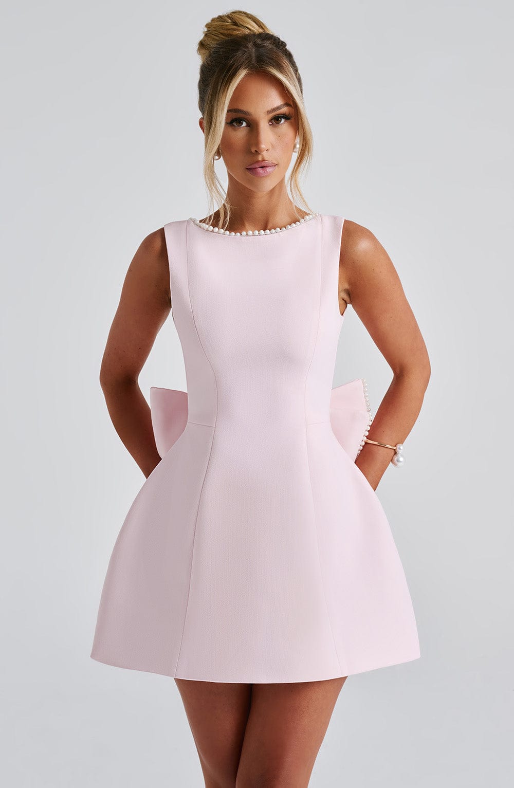 Front view of a light pink mini dress with a boat neck and pearl trim, featuring a structured A-line skirt.