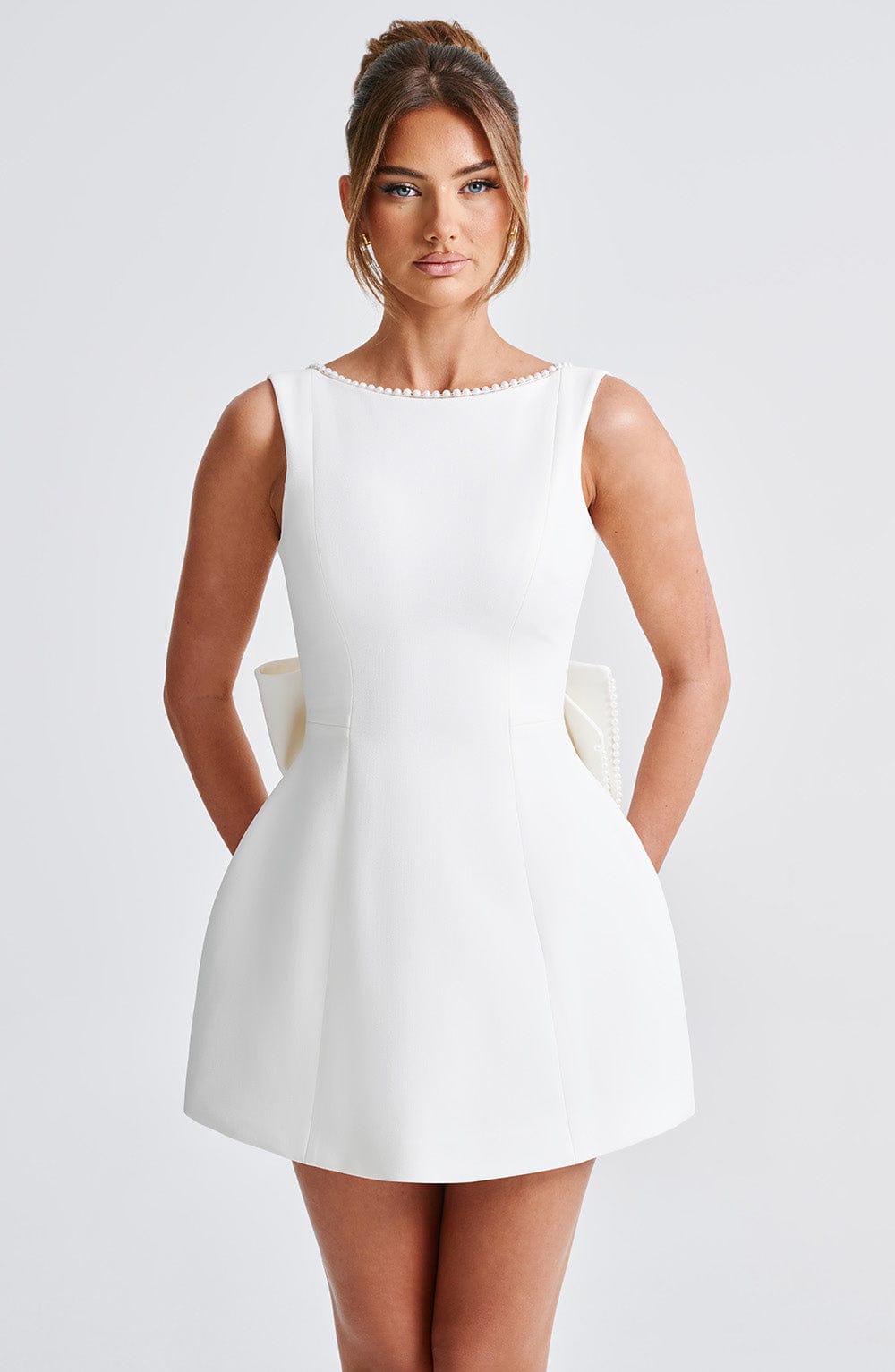 Front view of a white mini dress with a pearl-trimmed boat neckline, sleeveless design, and a structured silhouette.