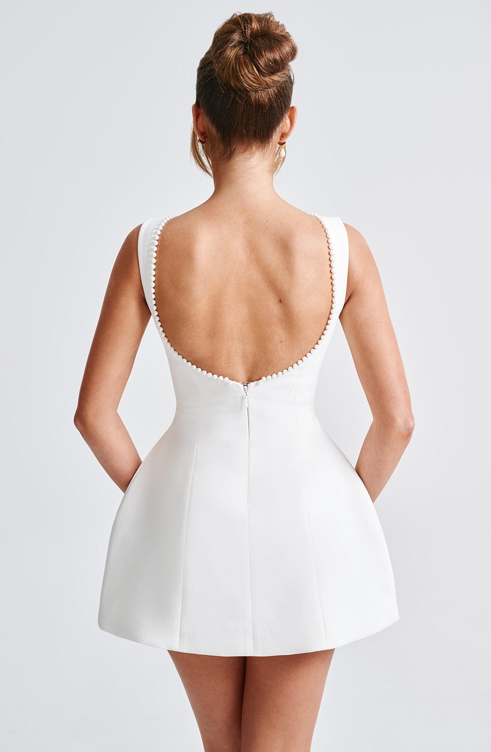 Back view of a white mini dress, showing the low scooped back with pearl trim and a subtle back zipper closure.