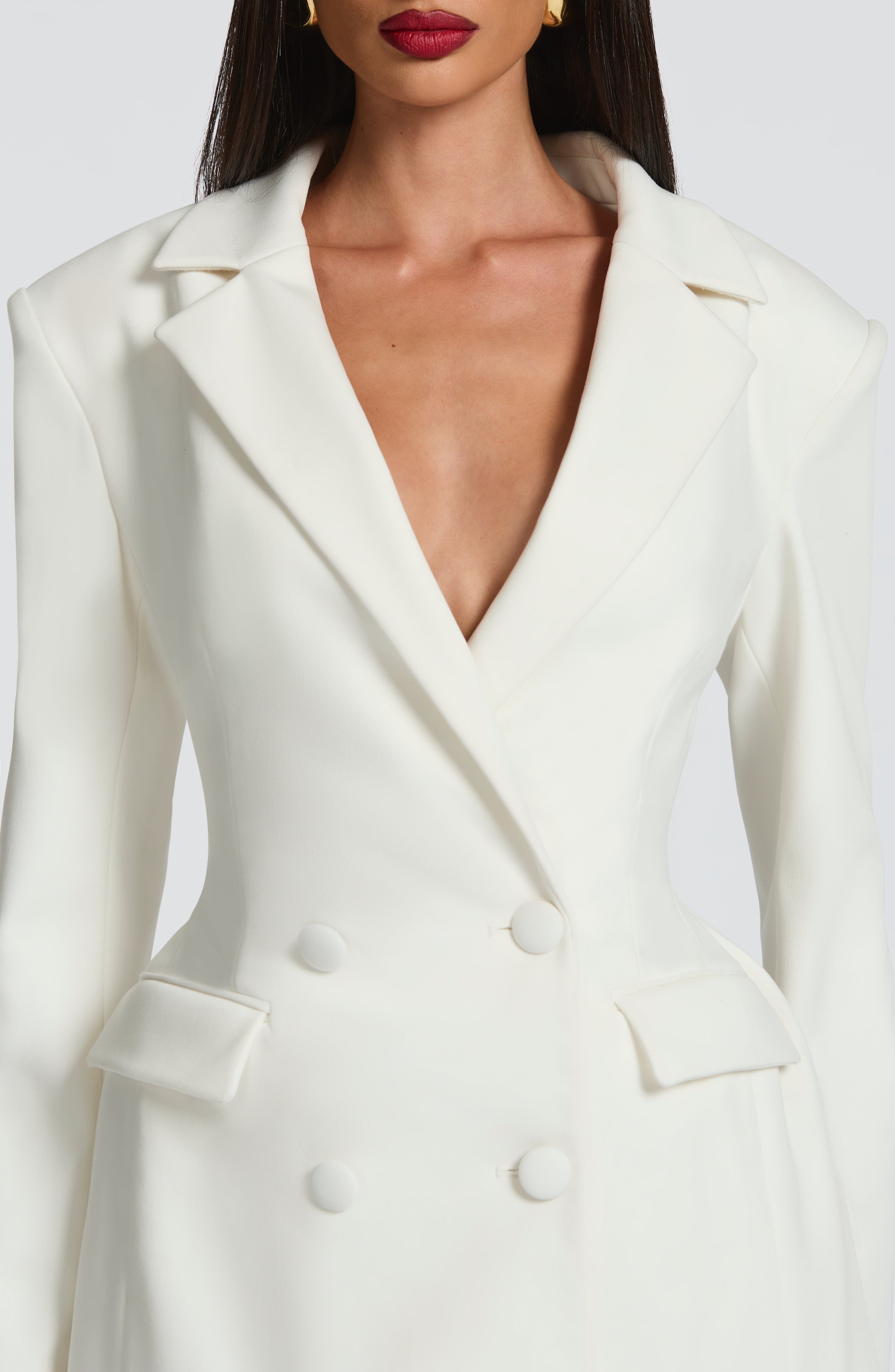 Close-up of the bodice of a white blazer mini dress, showing the double-breasted buttons and deep V-neck.