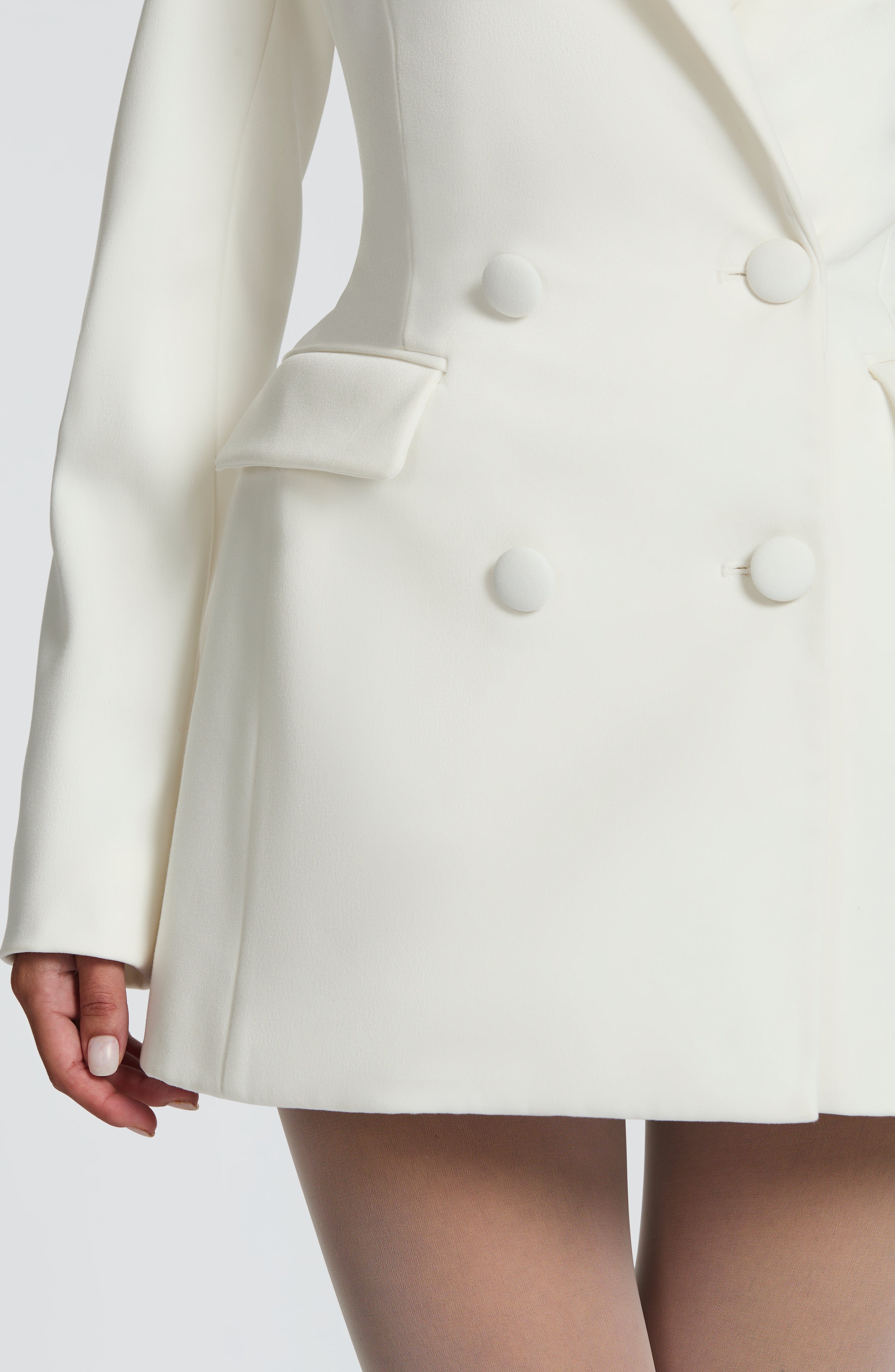 Side view of the lower half of a white blazer mini dress, highlighting the flap pockets and tailored hem.