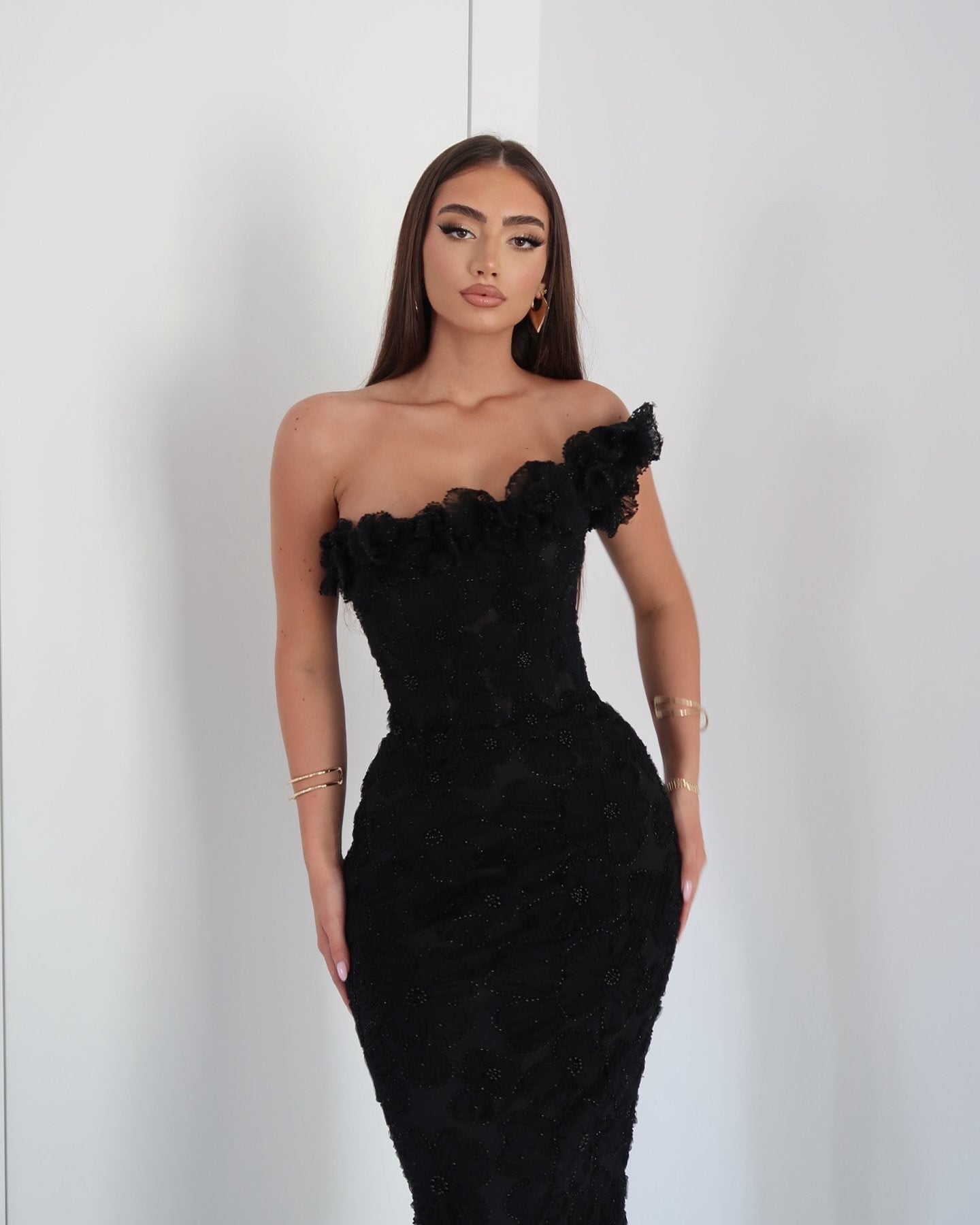 Close-up of a woman in a black one-shoulder maxi dress with ruffled floral details and beading for women.