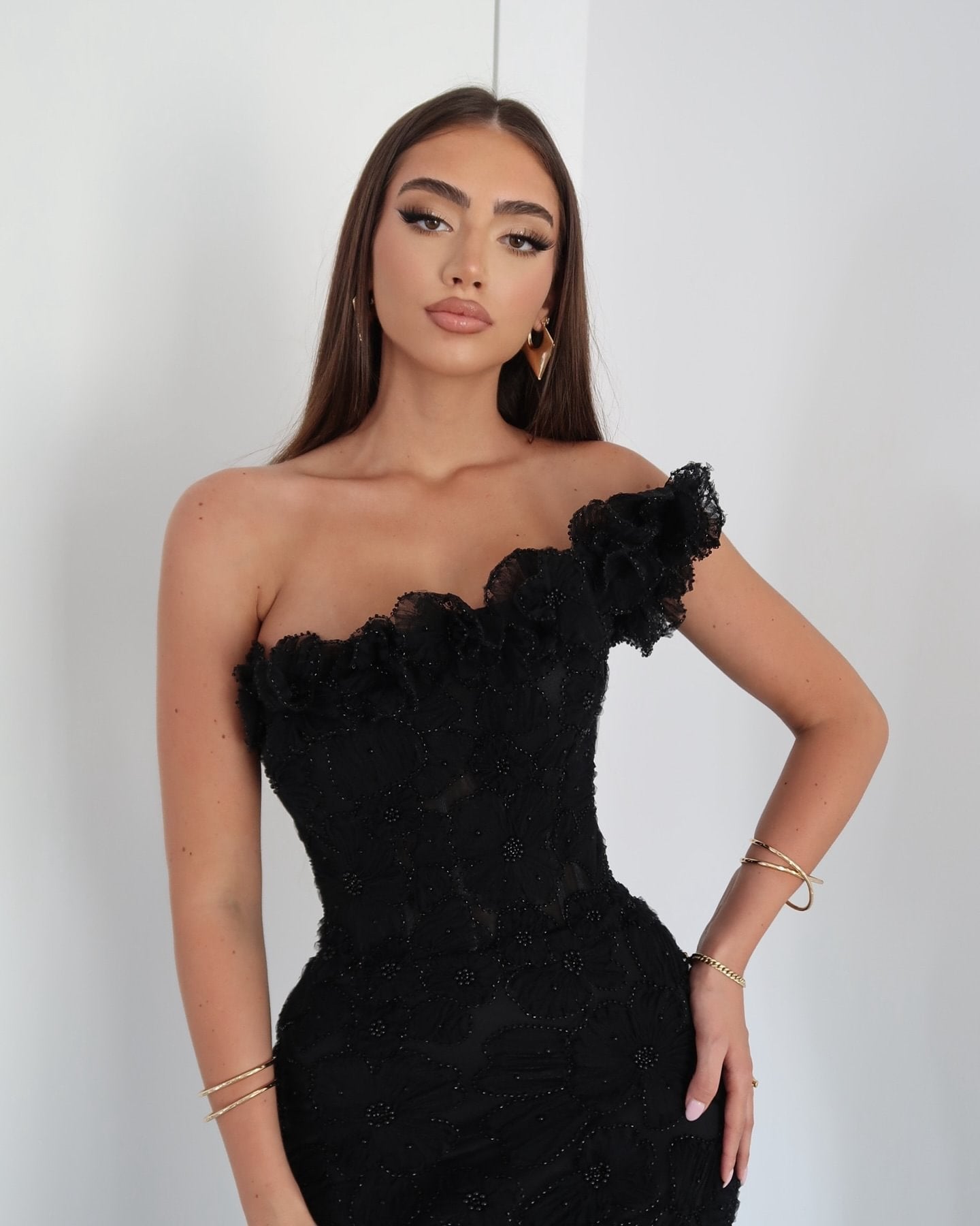 Front view of model posing in elegant black floral one-shoulder maxi dress with gold accessories for women.