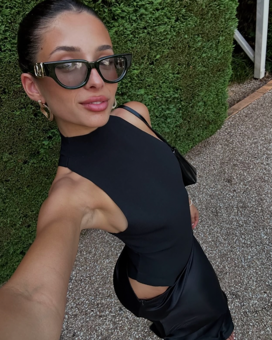 Close-up of a black cutout maxi dress, high neck, with black sunglasses and gold hoop earrings.
