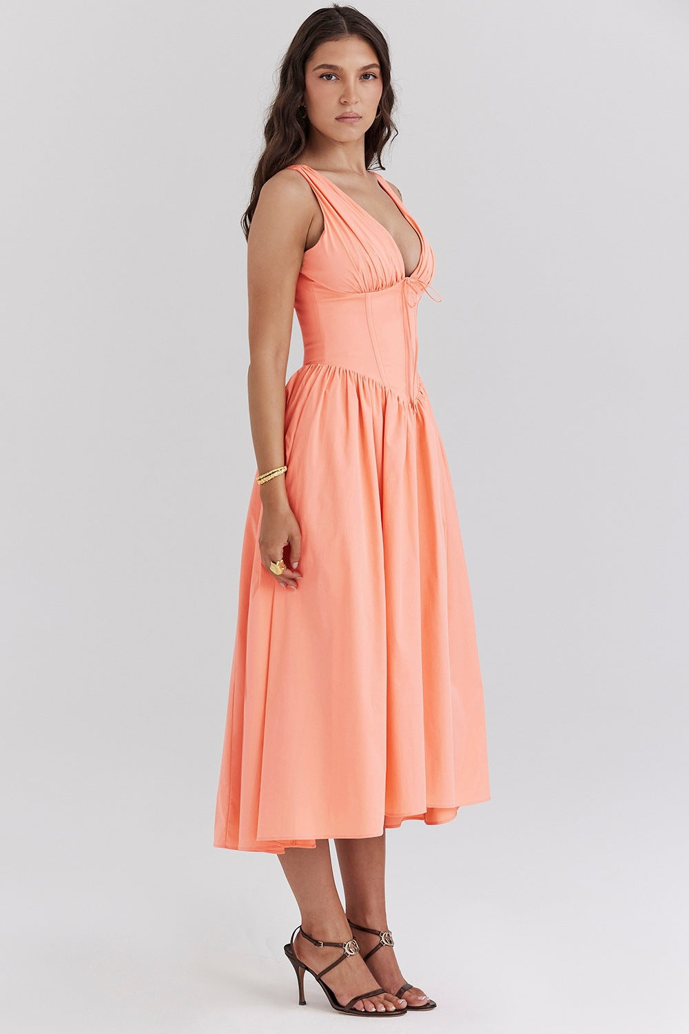 Side view of the peach Dahlia Midi Dress with a solid color, deep V-neck, and structured bodice, paired with brown heeled sandals.
