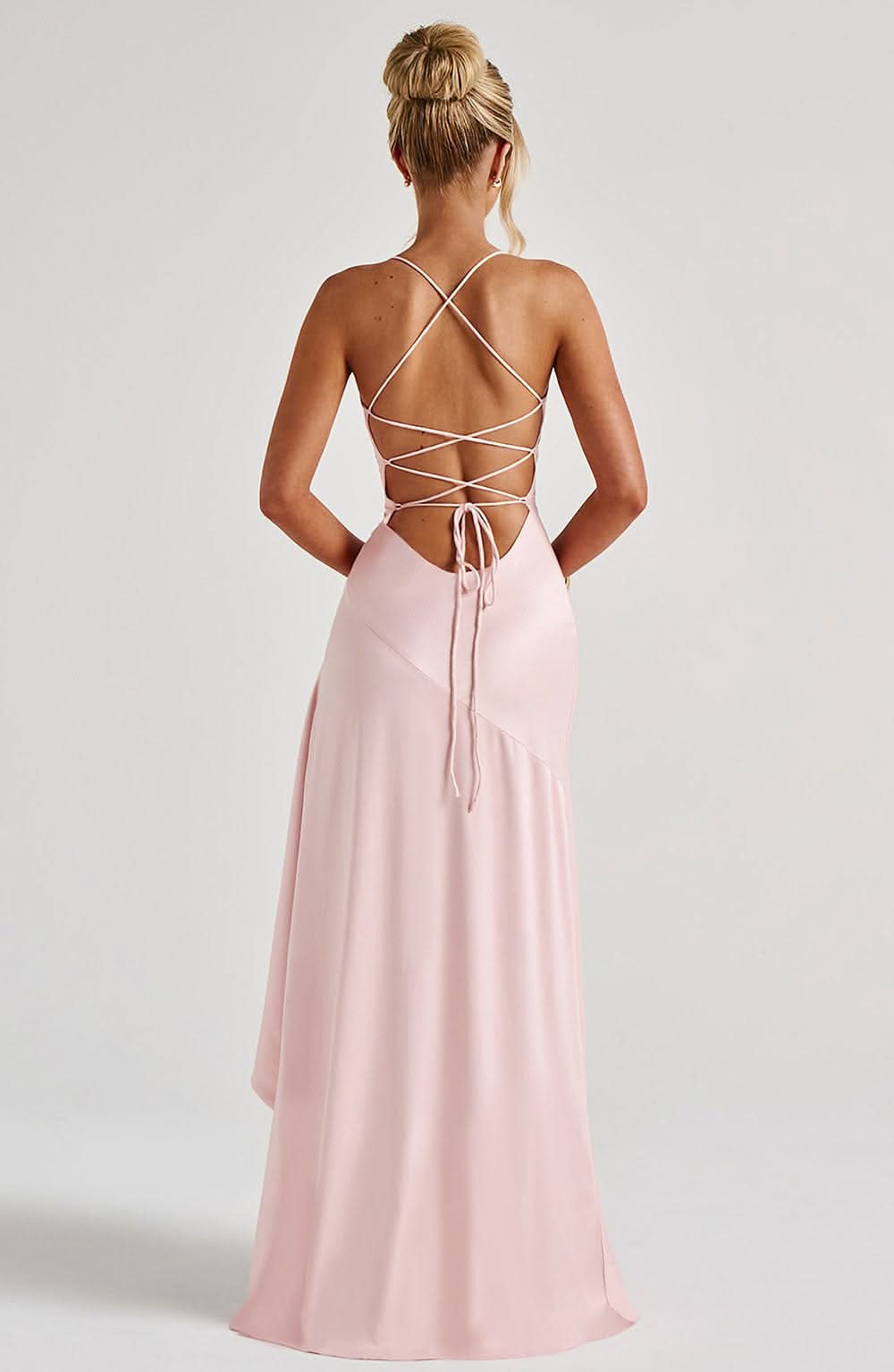 Back view of a light pink satin maxi dress, showing the criss-cross lace-up back detail and a full skirt.