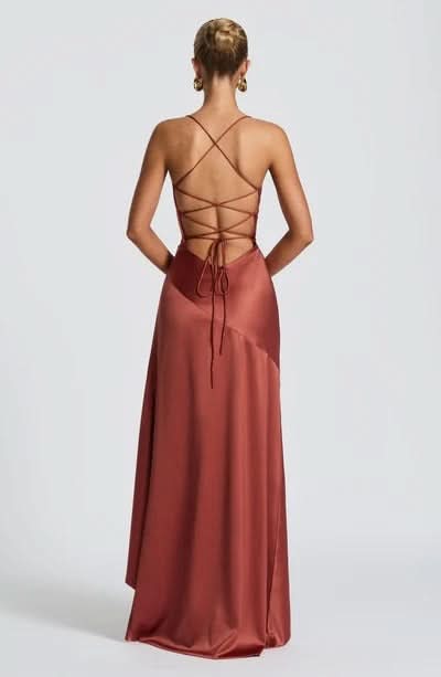 Back view of a rust-colored satin maxi dress with a criss-cross lace-up back design and flowing skirt.