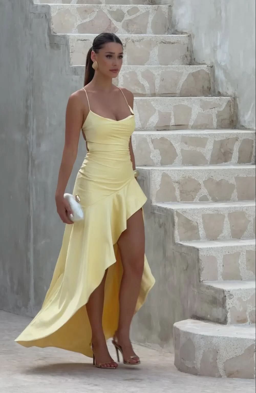 Woman walking in a yellow Daisy Ruffle Maxi Dress with a white clutch, showing the movement of the ruffled skirt.
