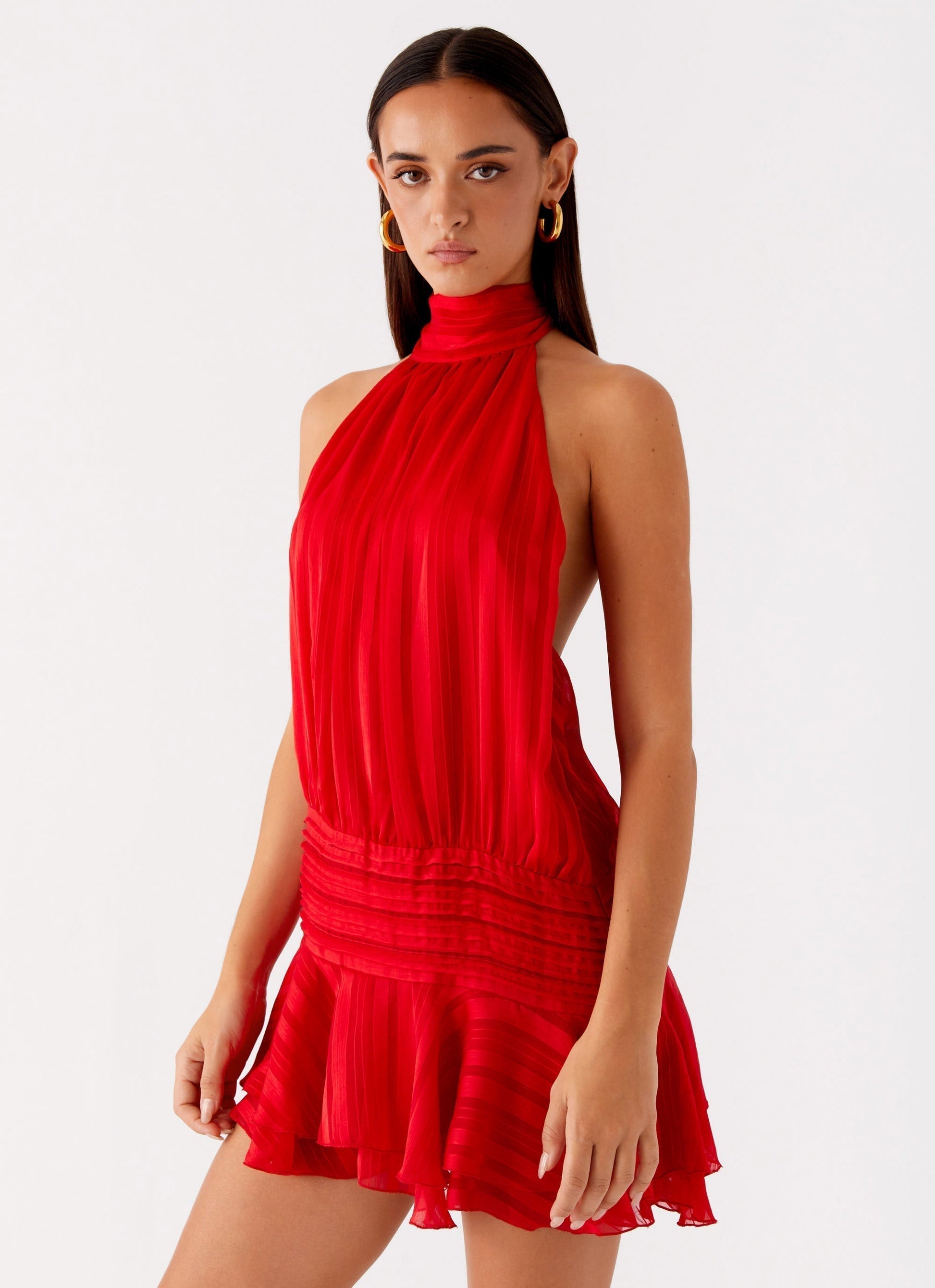 Vibrant red Daniela pleated mini dress, featuring a high halter neck and a cinched waist with a short, flowing skirt.