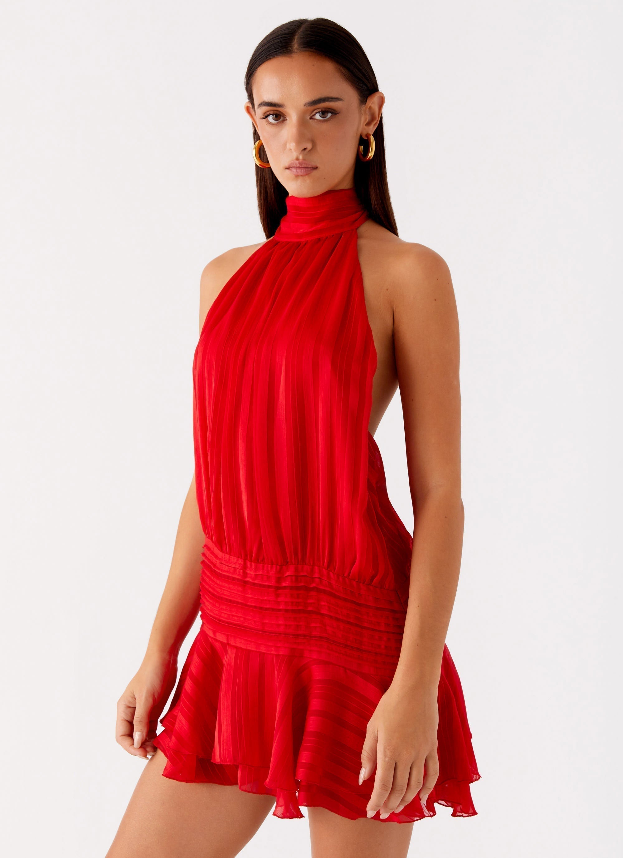 Vibrant red Daniela pleated mini dress, featuring a high halter neck and a cinched waist with a short, flowing skirt.