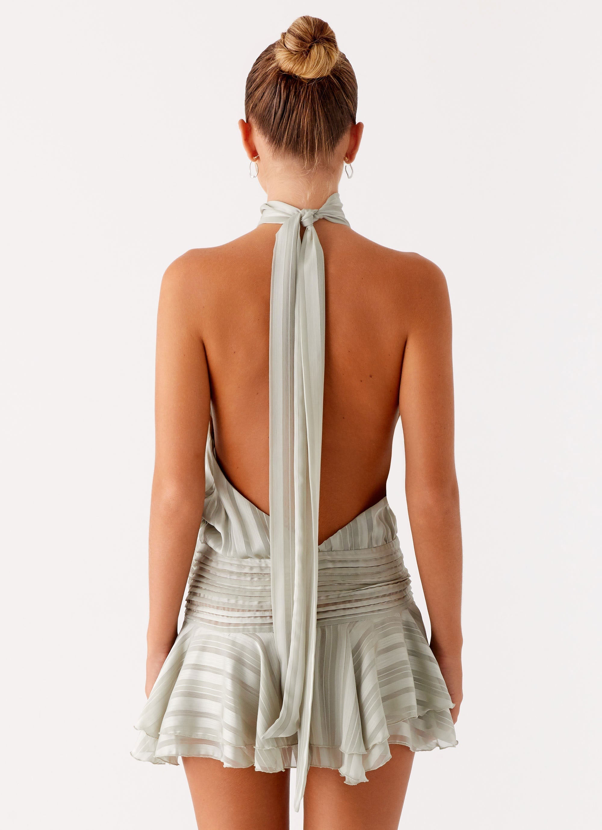 Back view of the sage green Daniela pleated mini dress, displaying the open back and long scarf-like neck tie.