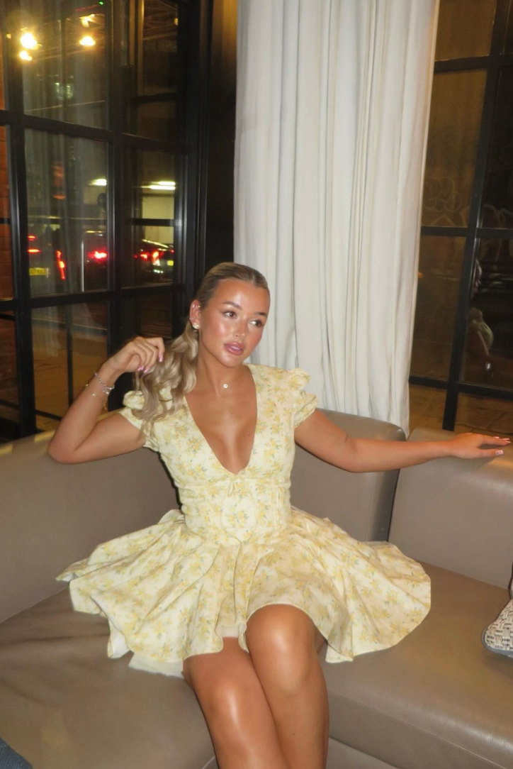 Cream mini dress with yellow floral pattern, short puff sleeves, and a full pleated skirt, relaxing on a sofa.