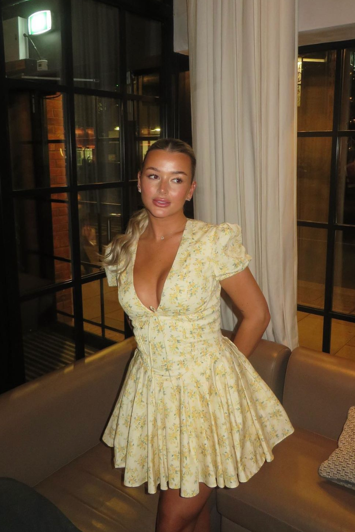 Side view of the Delaney pleated mini dress, showcasing the fitted bodice and voluminous pleated skirt in yellow floral print.