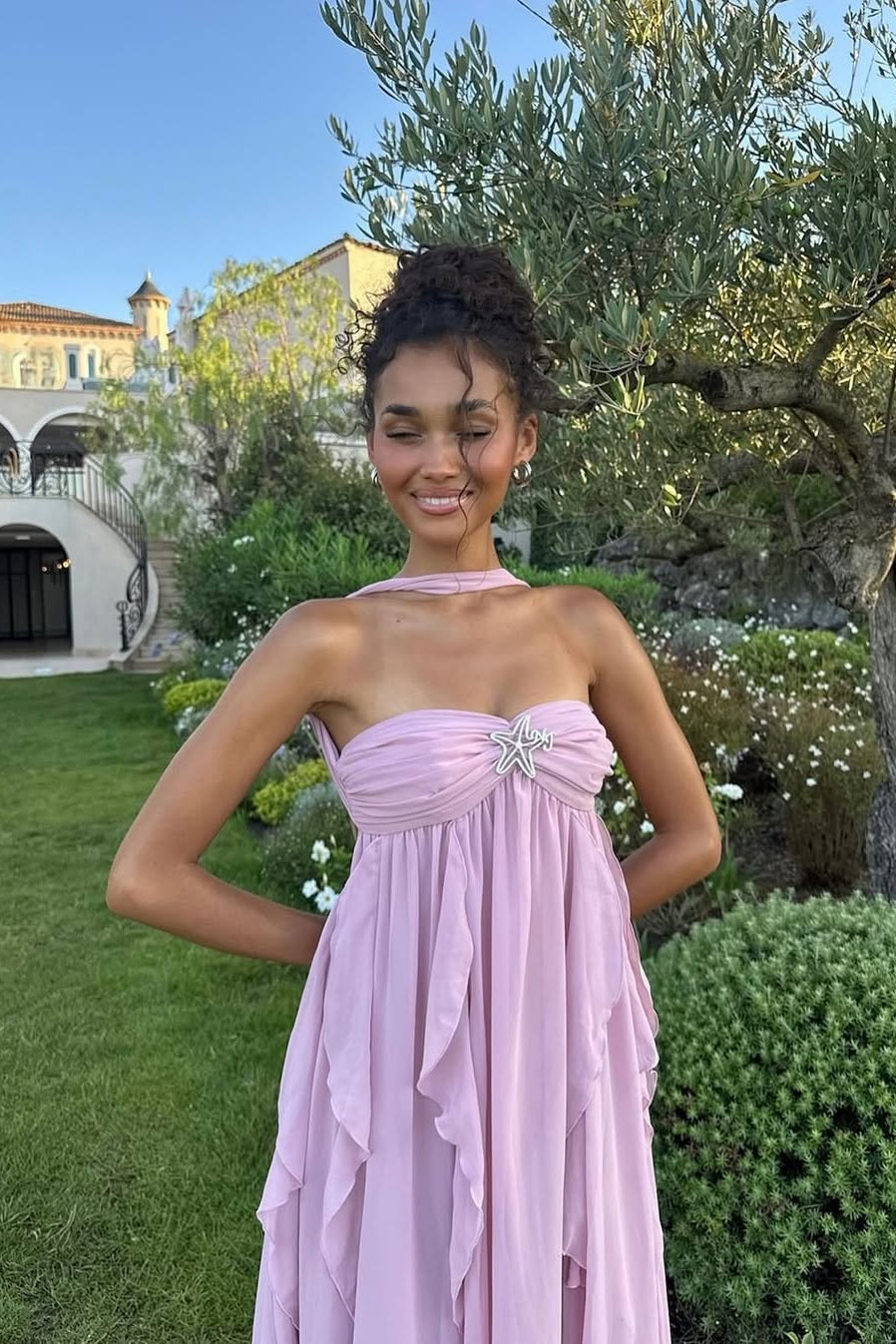 Light pink ruched maxi dress with a strapless bodice, halter neck tie, and flowing ruffled skirt, worn outdoors.