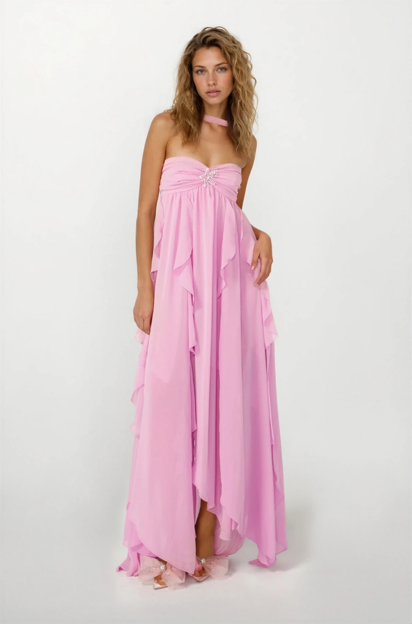 Full-length view of a pink ruched maxi dress with a sweetheart neckline, starfish brooch, and layered ruffles.