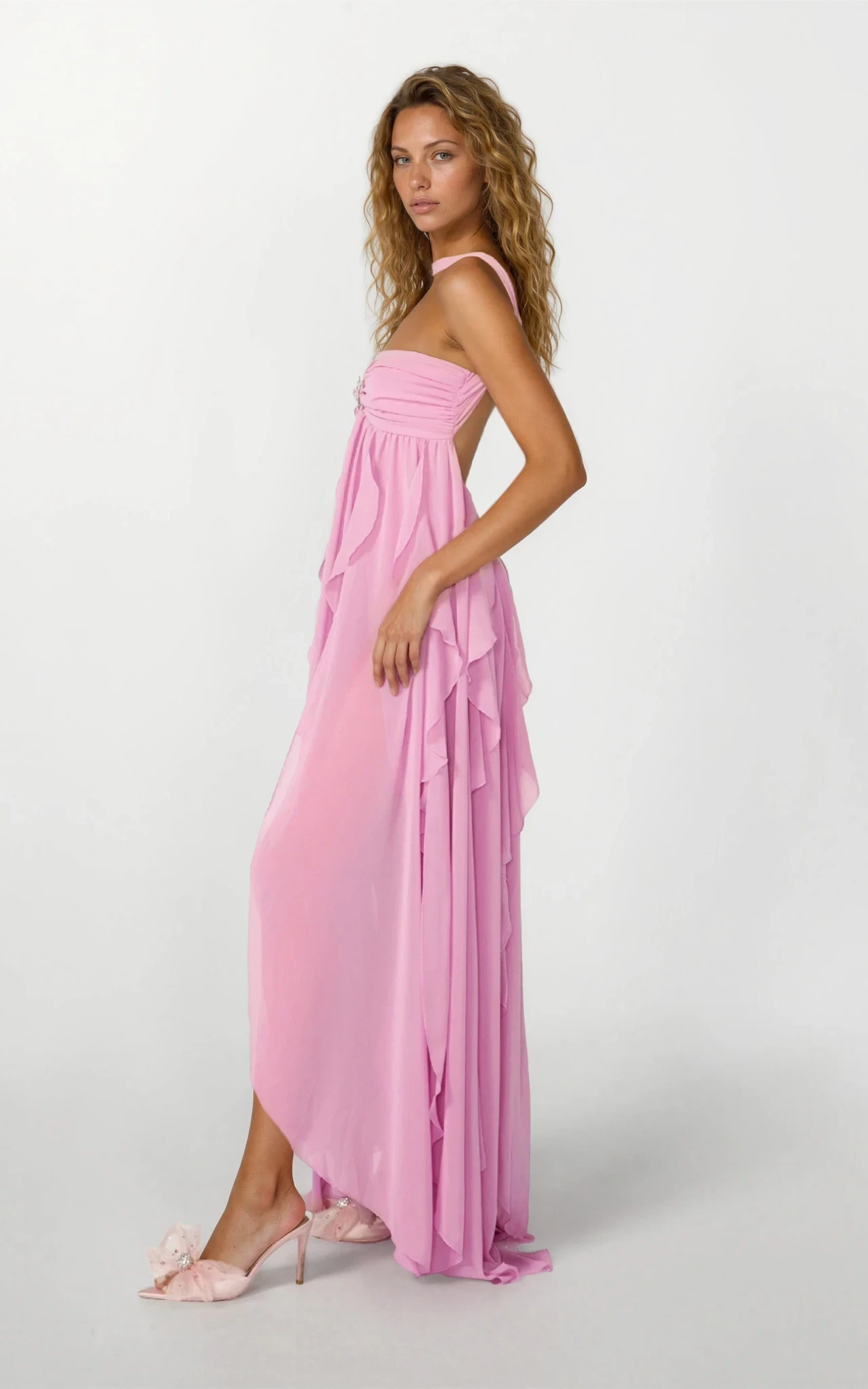 Side profile of a pink ruched maxi dress with a strapless bodice, halter neck, and cascading ruffled skirt.